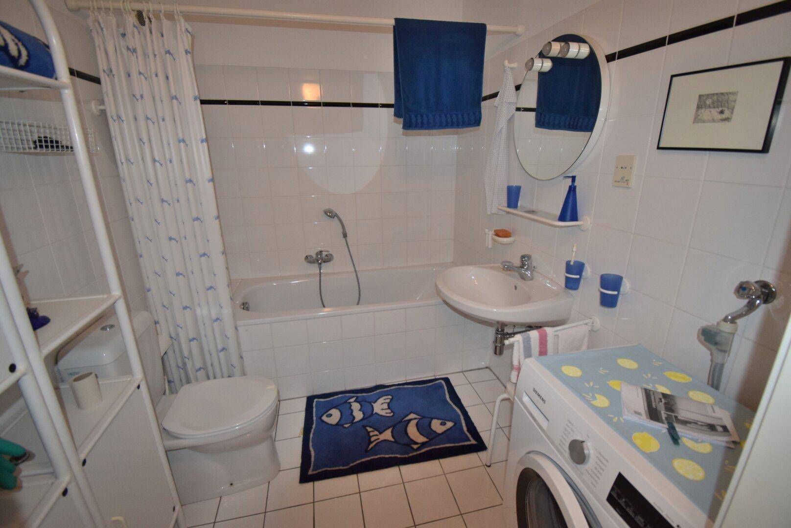 Funktionales Badezimmer mit Badewanne, Waschbecken, WC und Waschmaschine.
