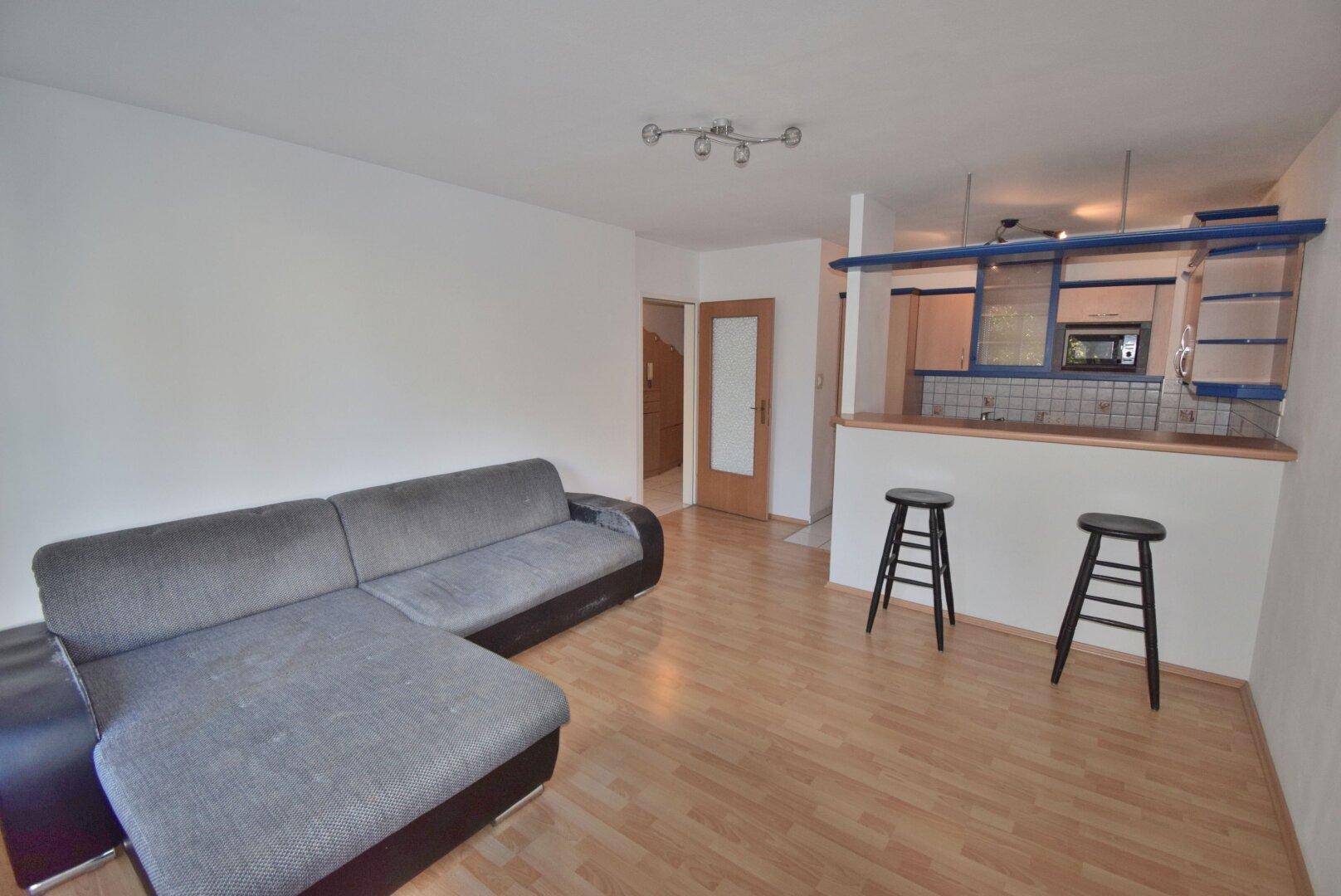 Offener Wohnbereich mit Laminatboden, Sofa und einer Frühstücksbar, die zur Küche führt.
