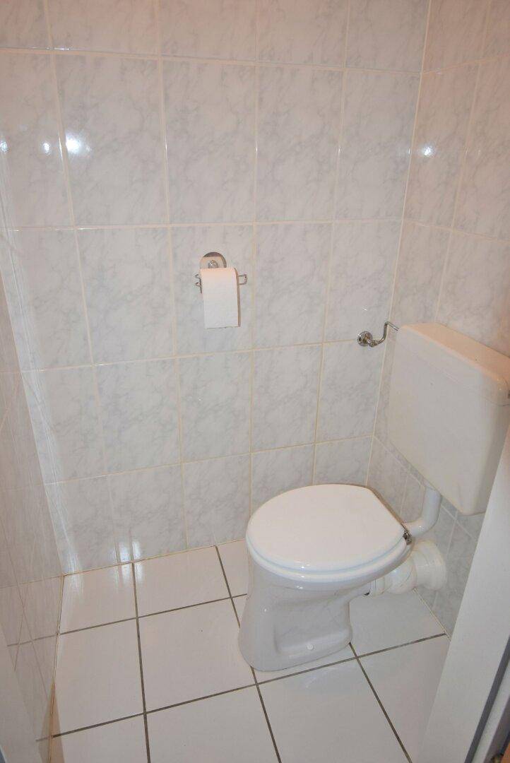 Separates WC mit weißen Wand- und Bodenfliesen und einer Standardtoilette.