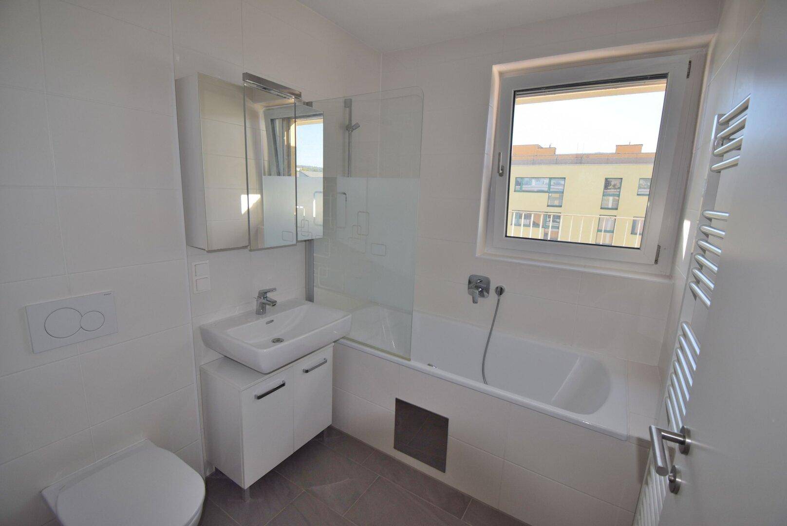 Modernes Badezimmer mit Badewanne, Waschbeckenunterschrank und beheiztem Handtuchhalter.