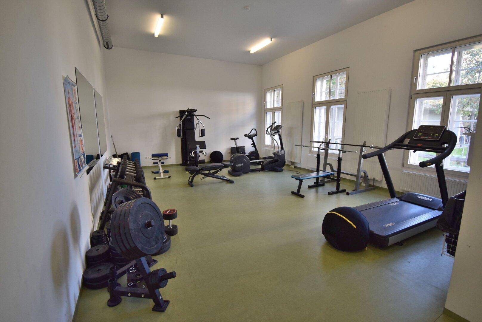 Gut ausgestatteter Fitnessraum mit verschiedenen Trainingsgeräten und natürlichem Lichteinfall.