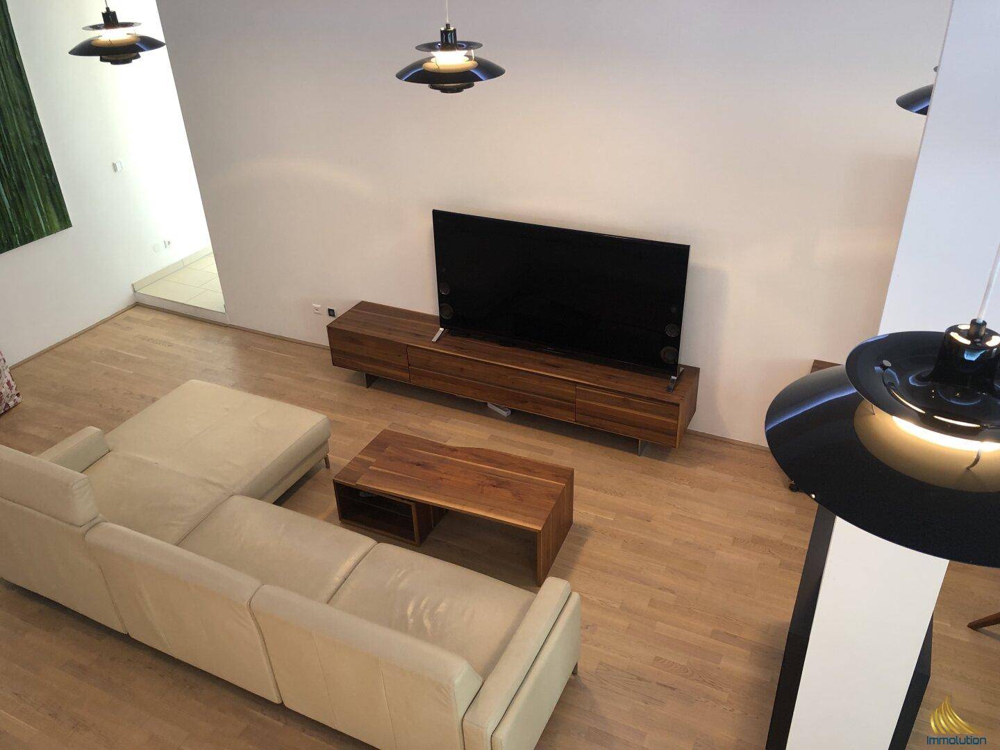 Blick von oben auf den hellen Wohnbereich mit großem Sofa, Holzboden und modernem TV-Möbel.
