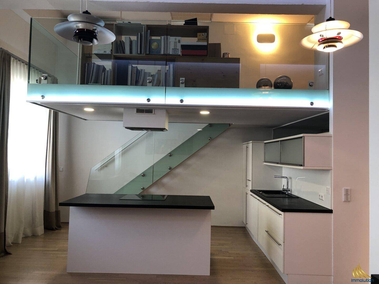 Moderne Küche mit Kochinsel, weißen Schränken und einer eleganten Glasbrüstung zur oberen Ebene.