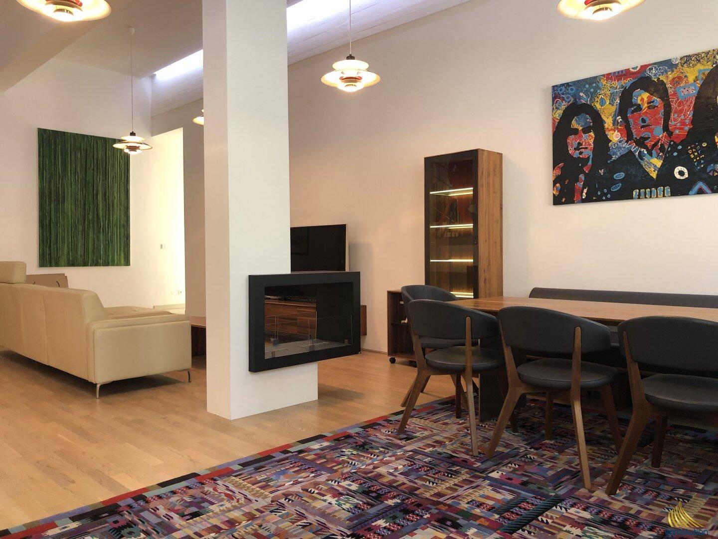Offener Wohn- und Essbereich mit Holzboden, modernem Kamin und farbenfroher Kunst an der Wand.