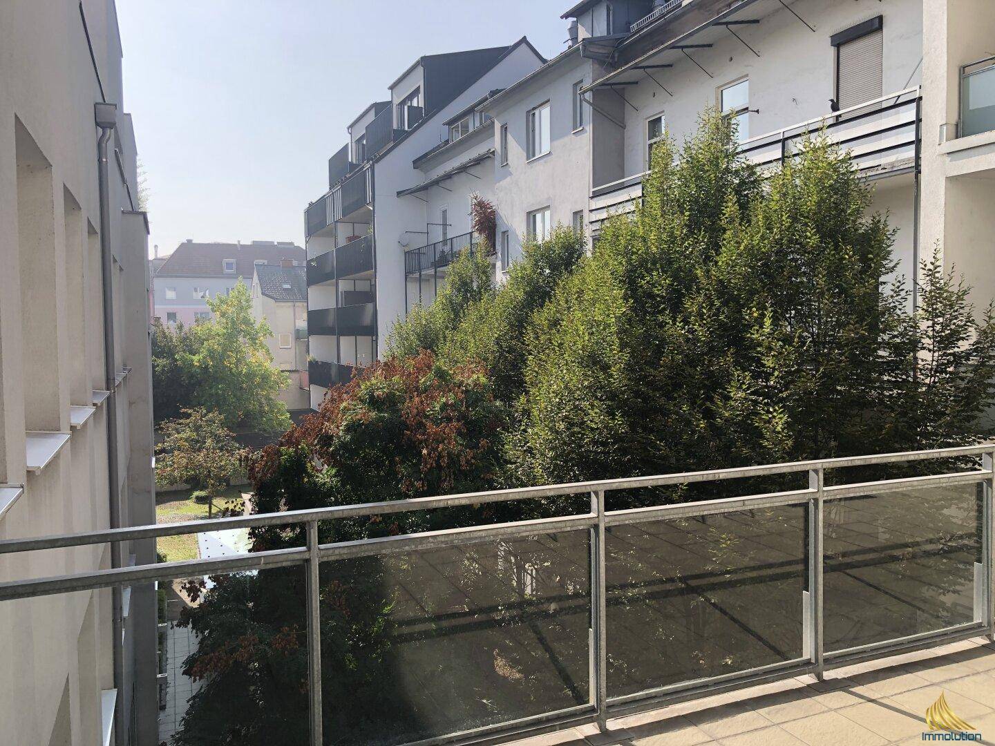 Balkon mit Blick auf einen grünen Innenhof und umliegende Wohngebäude.
