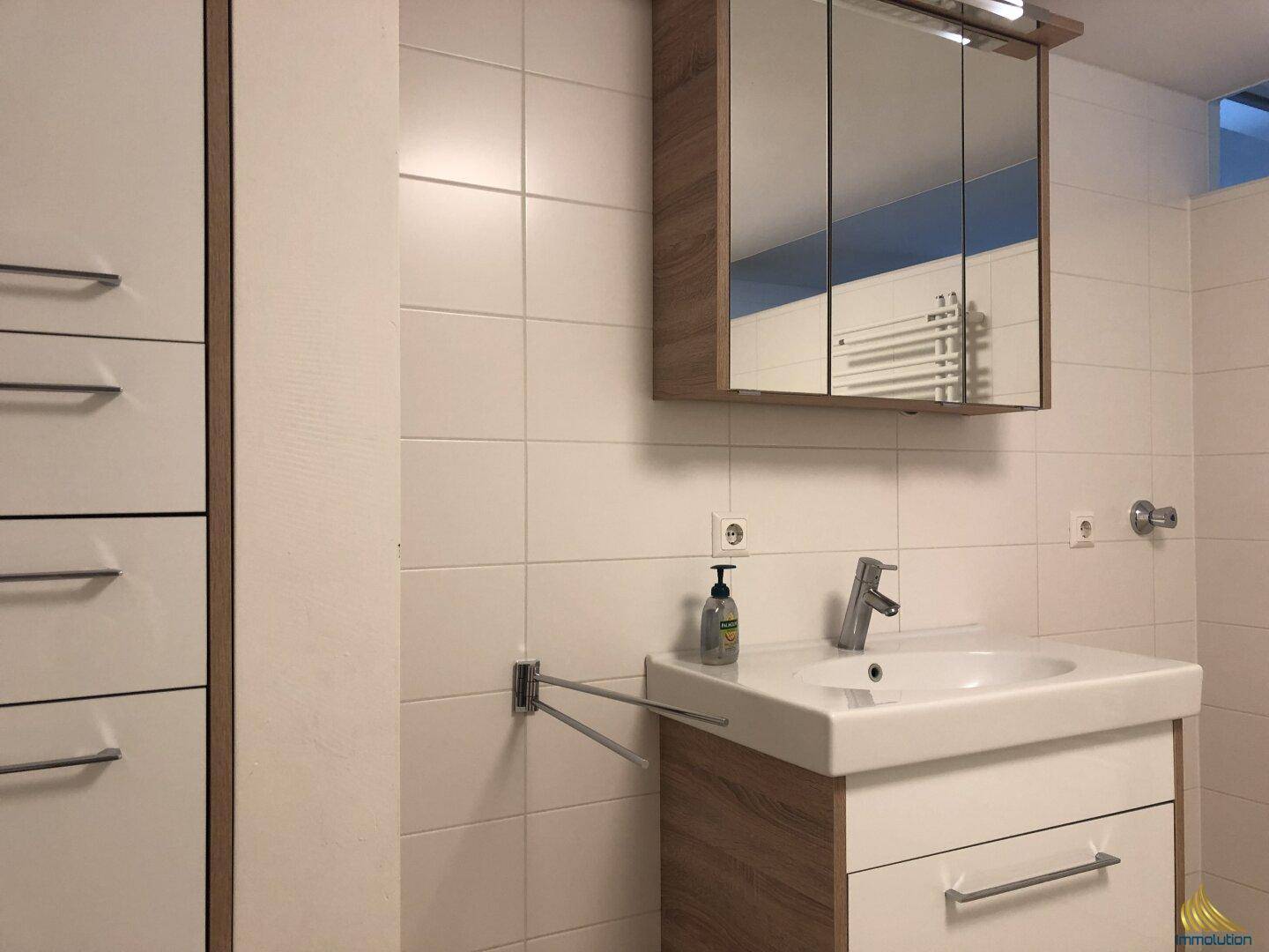 Modernes Badezimmer mit Einzelwaschbecken, Spiegelschrank und weißen Wandfliesen.