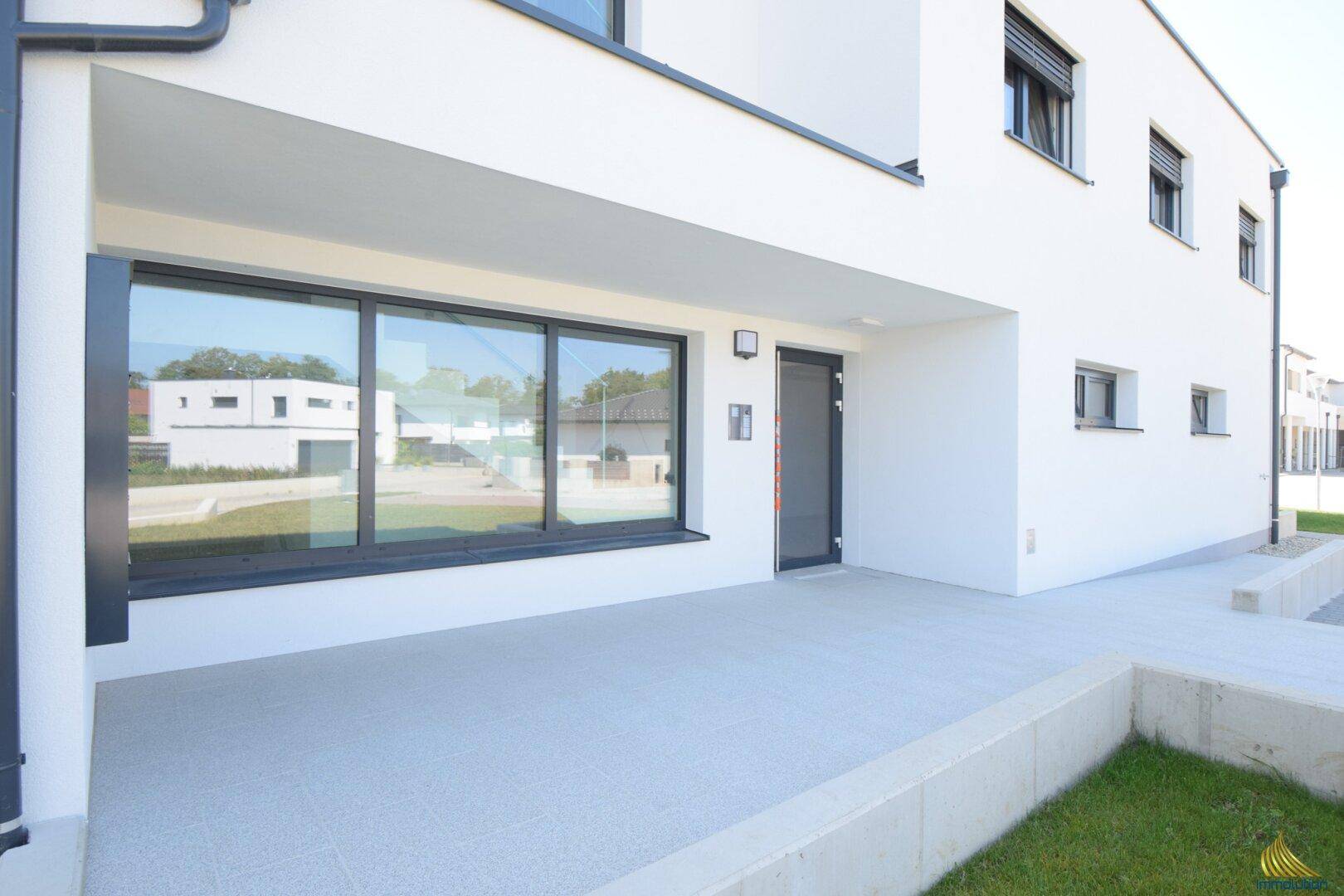Erdgeschoss-Terrasse mit Fliesenboden und großzügigen Fenstern zur Wohnanlage, sonnig und einladend.