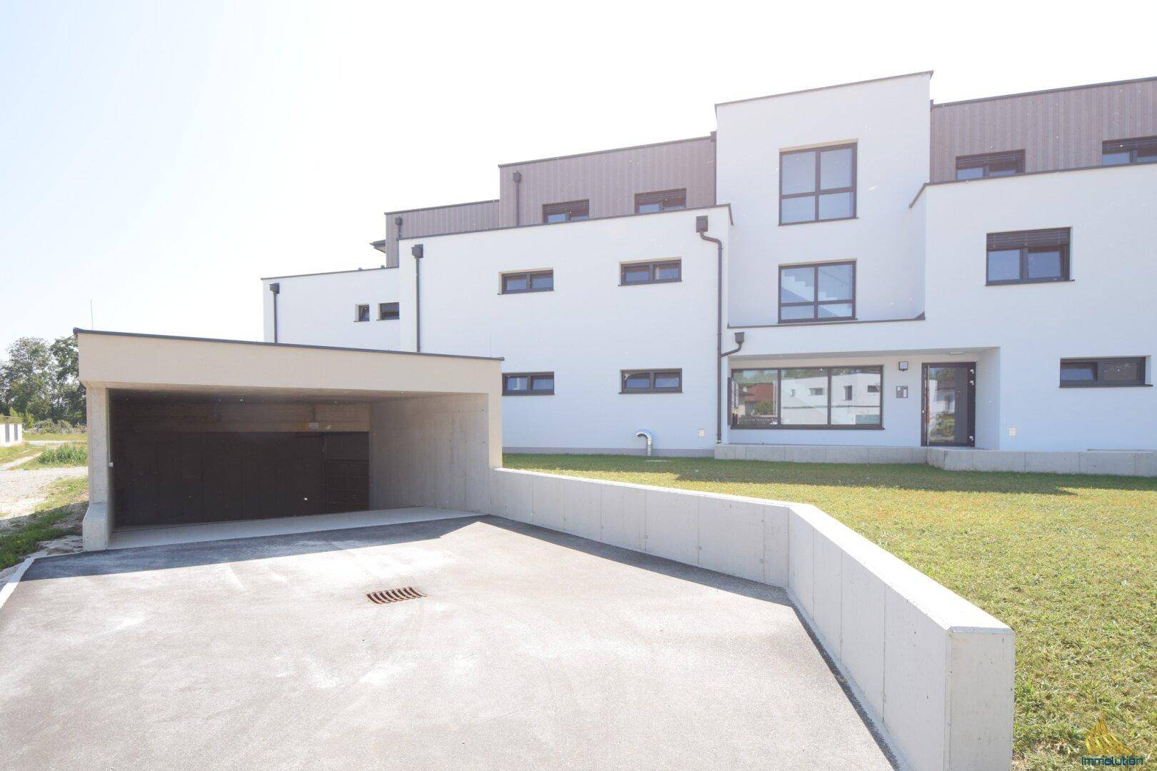 Moderne Wohnanlage mit weißer Fassade und Zufahrt zu einer Tiefgarage.