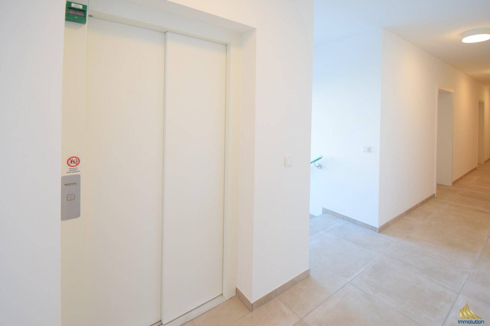 Heller Flur in einem Mehrfamilienhaus mit Aufzug und modernem Fliesenboden.