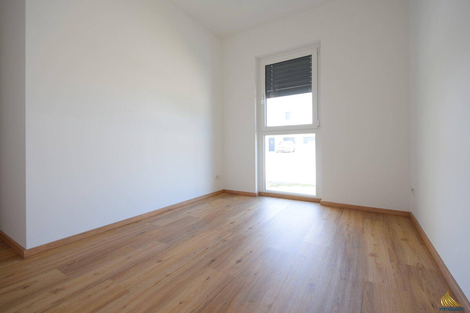 Leeres Schlafzimmer mit hellem Laminatboden und einem Fenster, bereit zur individuellen Gestaltung.
