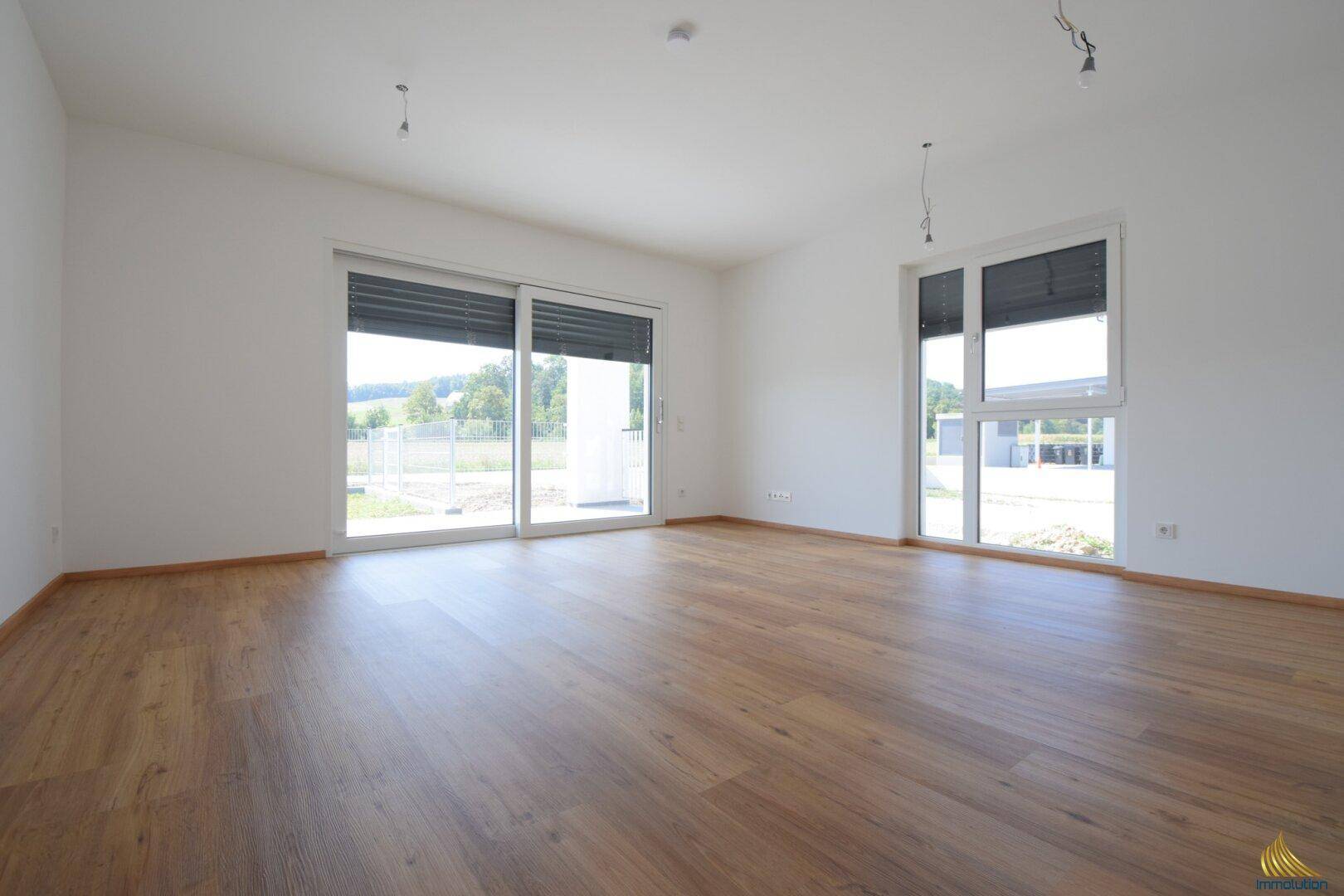 Helles, leeres Wohnzimmer mit modernem Laminatboden und Zugang zu einem Außenbereich.