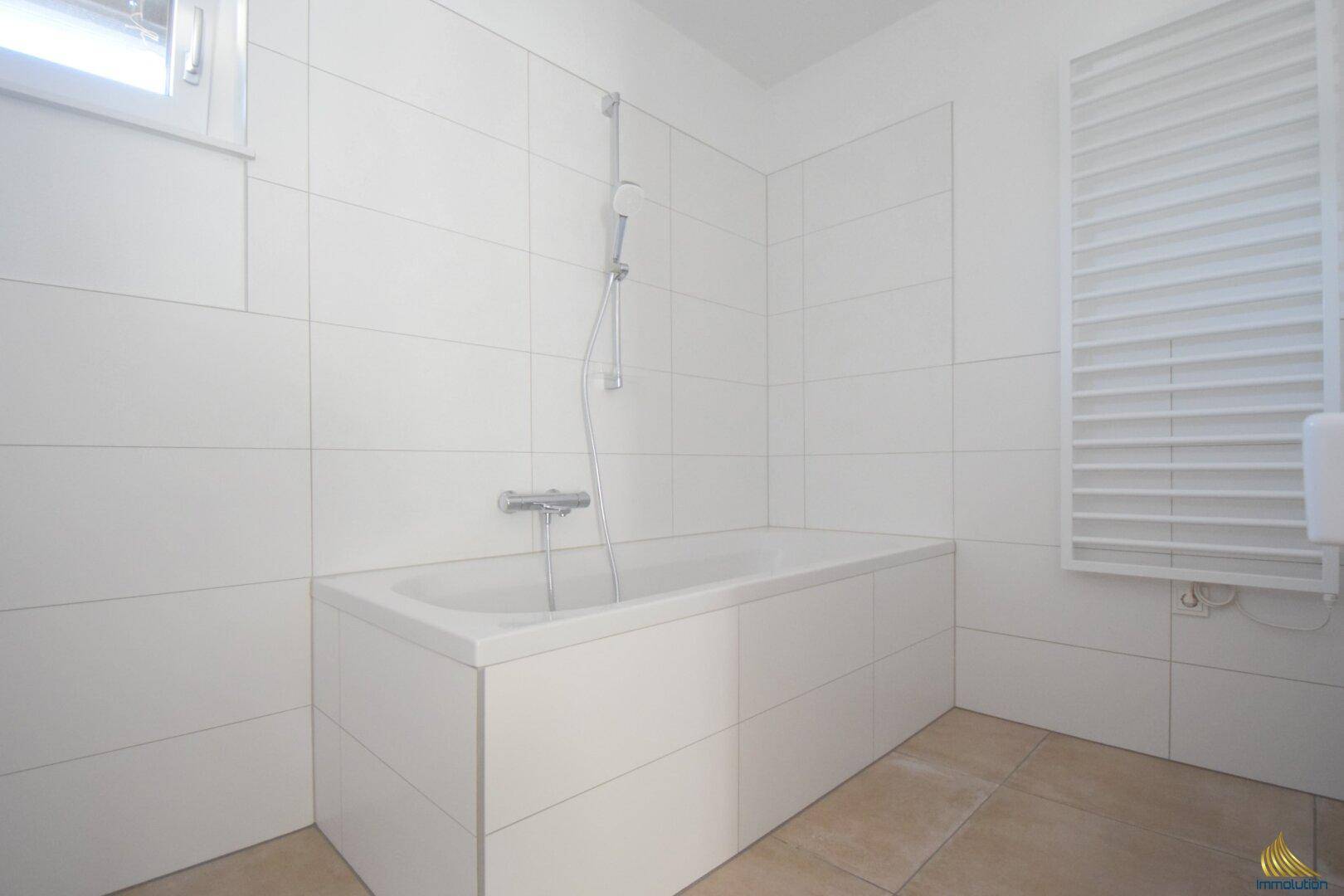 Modernes Badezimmer mit Badewanne, weißen Fliesen und praktischem Handtuchheizkörper.
