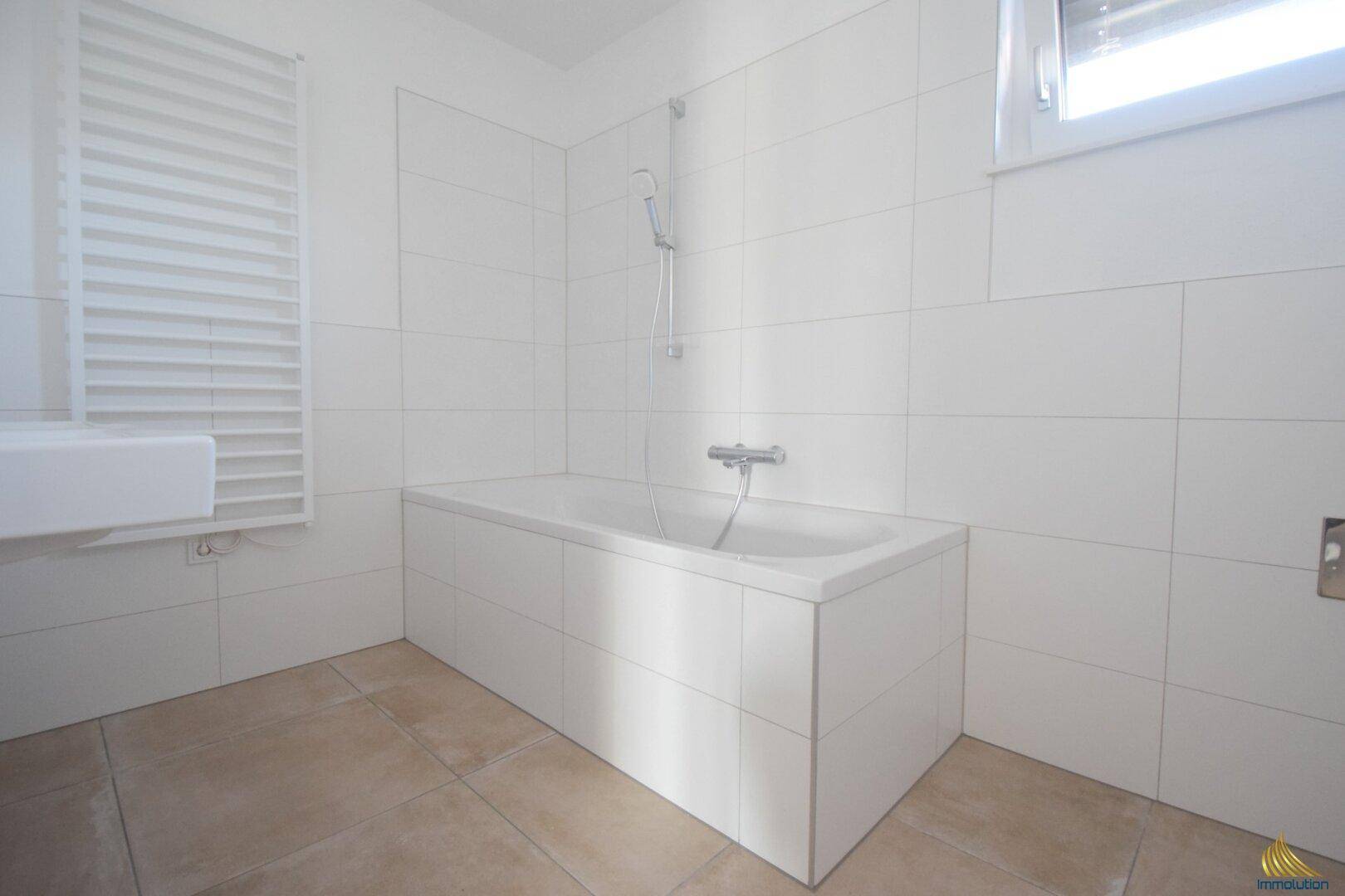 Modernes Badezimmer mit weiß gefliesten Wänden, Badewanne und beheiztem Handtuchhalter.