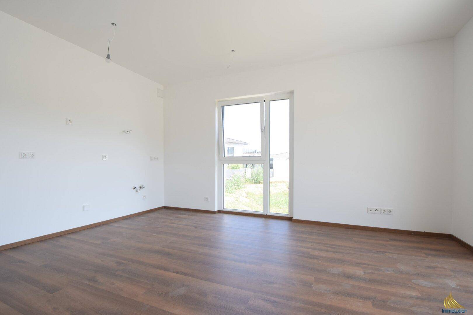 Leeres Schlafzimmer mit Laminatboden und großem Fenster, bietet viel Tageslicht und Blick ins Grüne.