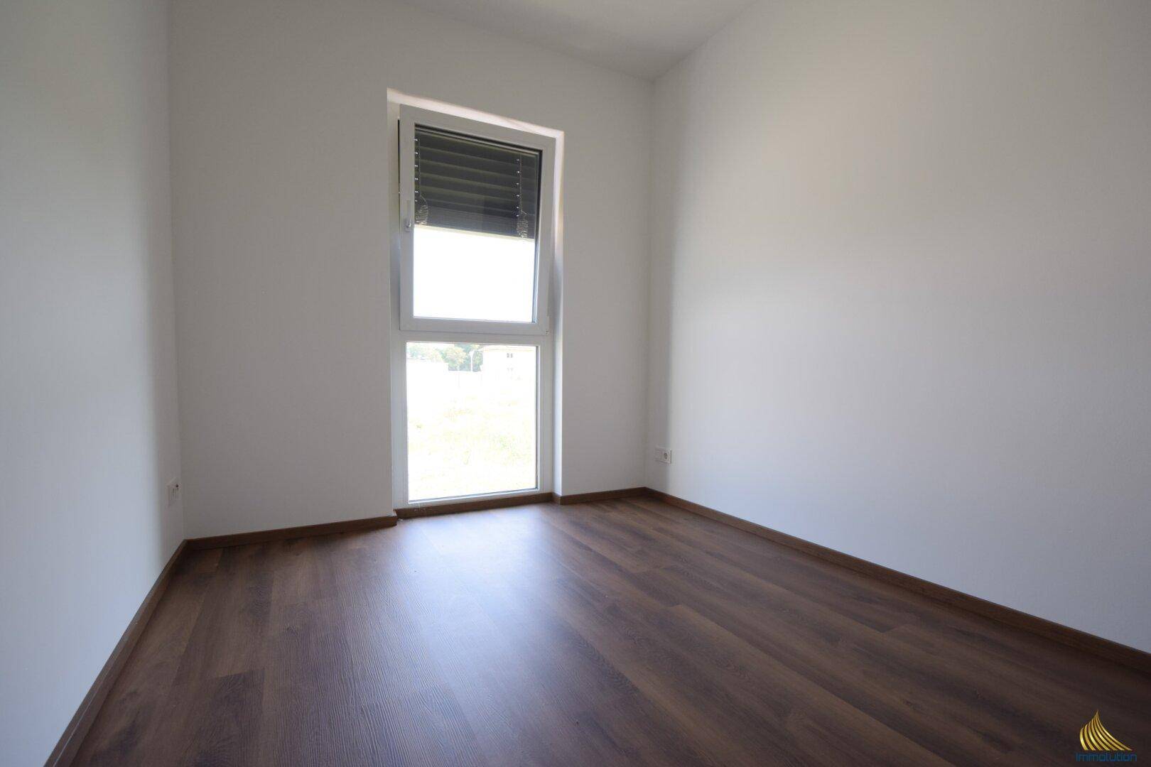 Helles, unmöbliertes Zimmer mit Laminatboden und Fenster, bietet vielseitige Nutzungsmöglichkeiten.