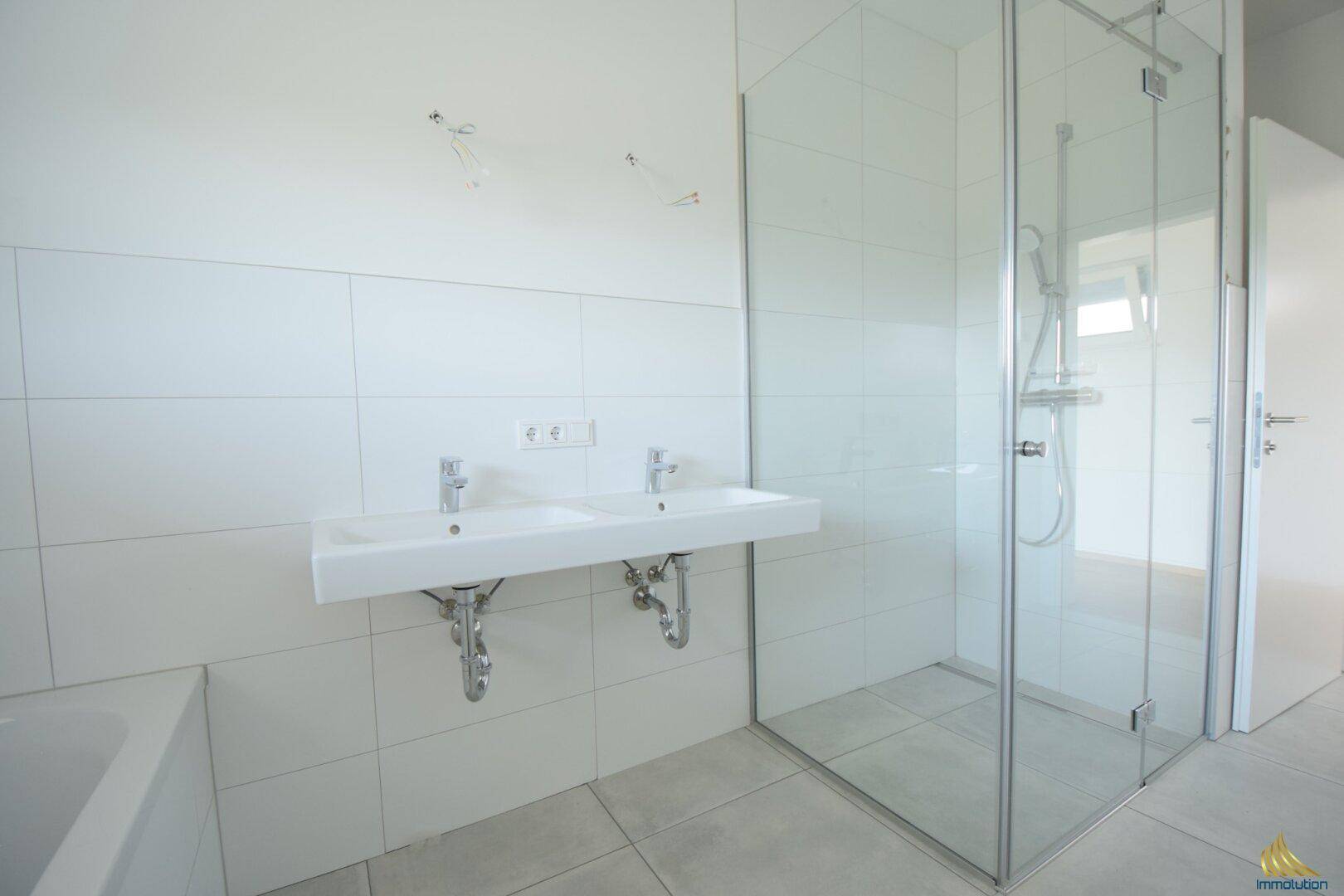 Helles Badezimmer mit großer Glasdusche, Doppelwaschbecken und weißen Fliesen.