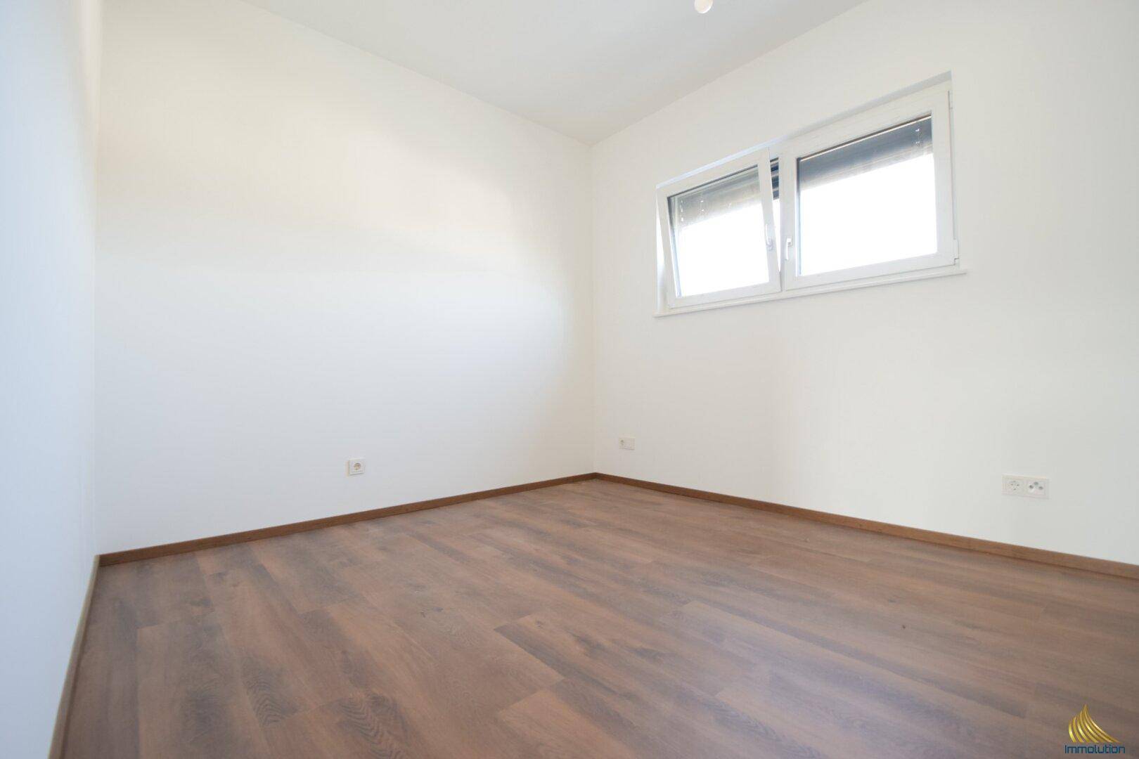 Unmöbliertes Schlafzimmer mit Laminatboden und einem Fenster mit Rollladen.