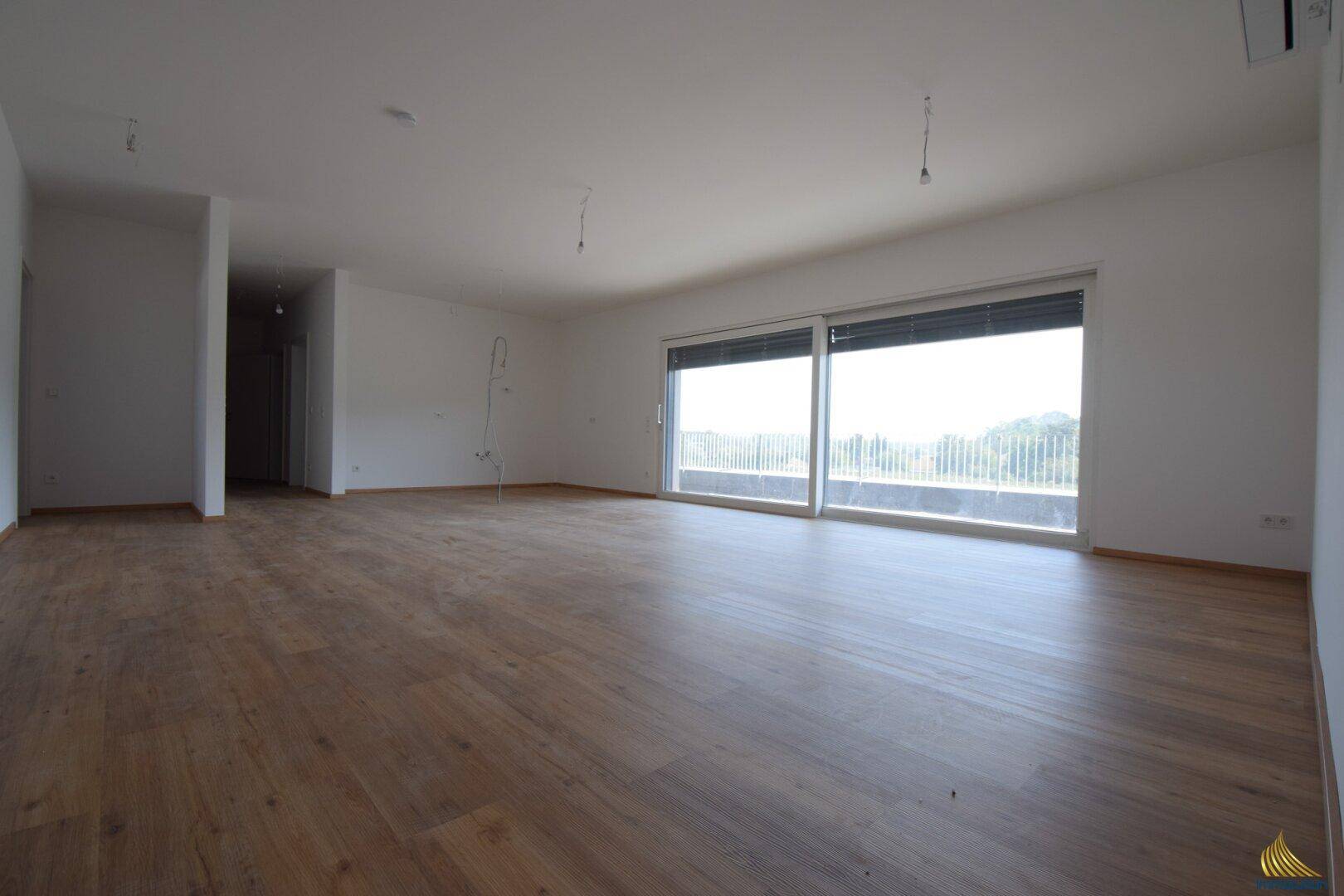 Geräumiges, unmöbliertes Wohnzimmer mit Laminatboden und Zugang zu einem Balkon.
