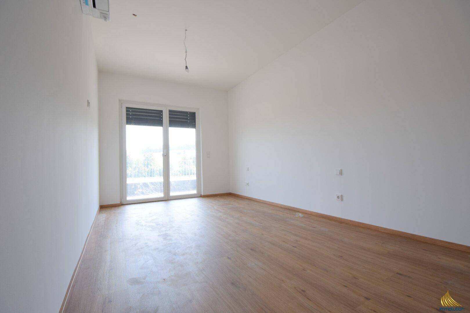 Helles Schlafzimmer mit Laminatboden und Zugang zu einem französischen Balkon.