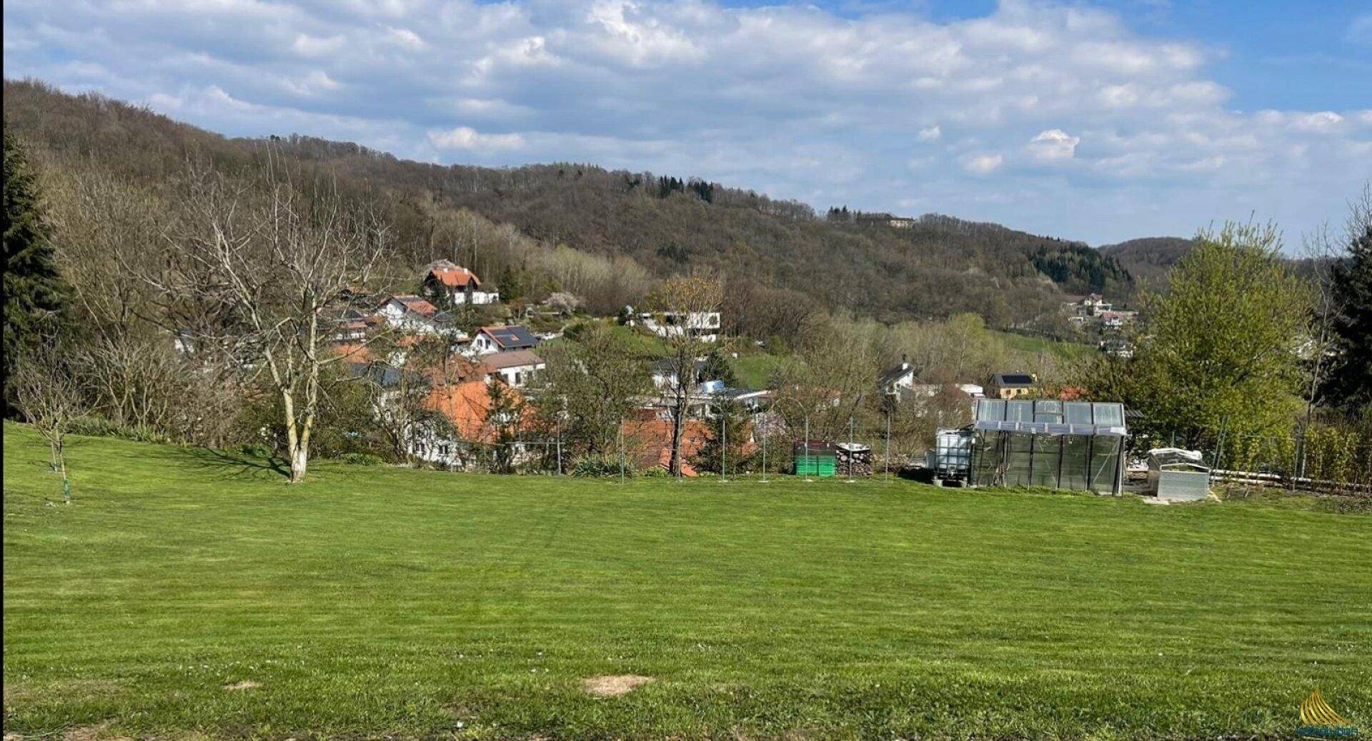 Weitläufige Grünfläche mit Blick auf ein malerisches Dorf und bewaldete Hügel in der Ferne.
