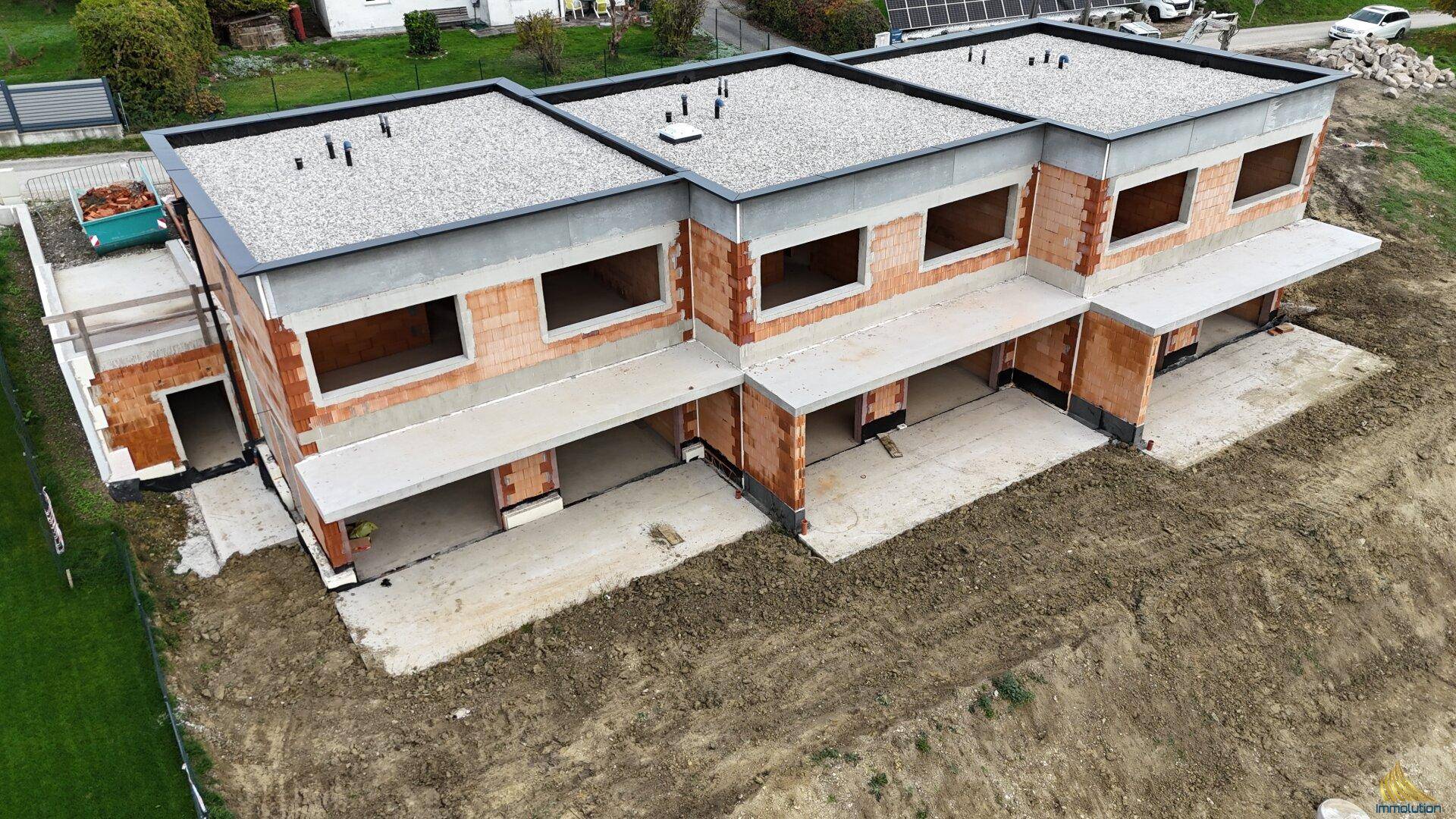Schrägansicht der im Bau befindlichen Reihenhäuser mit Rohbau und vorbereiteten Flachdächern.