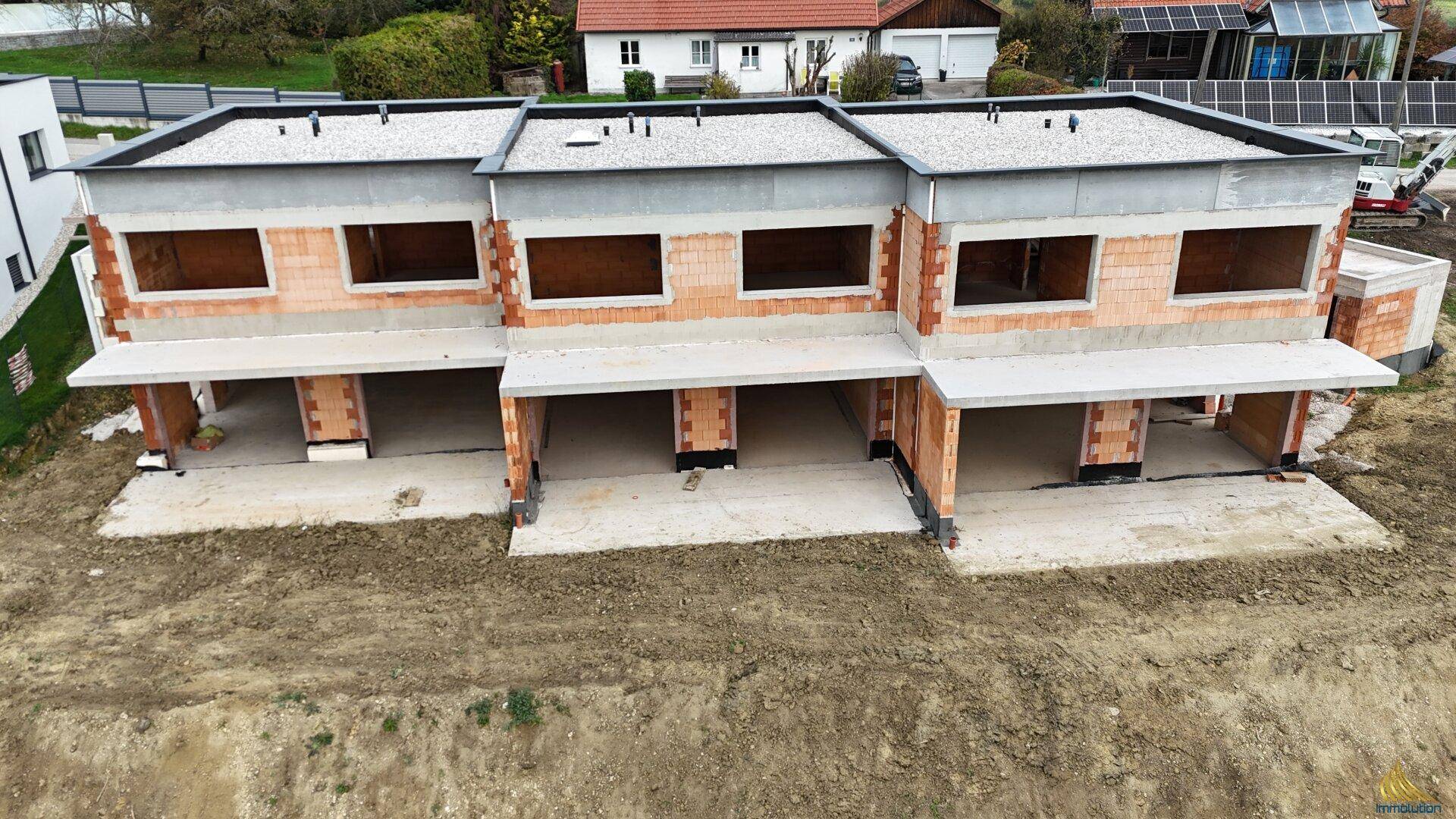 Nahaufnahme der im Bau befindlichen Reihenhäuser mit unverputzten Ziegelwänden und Flachdächern.
