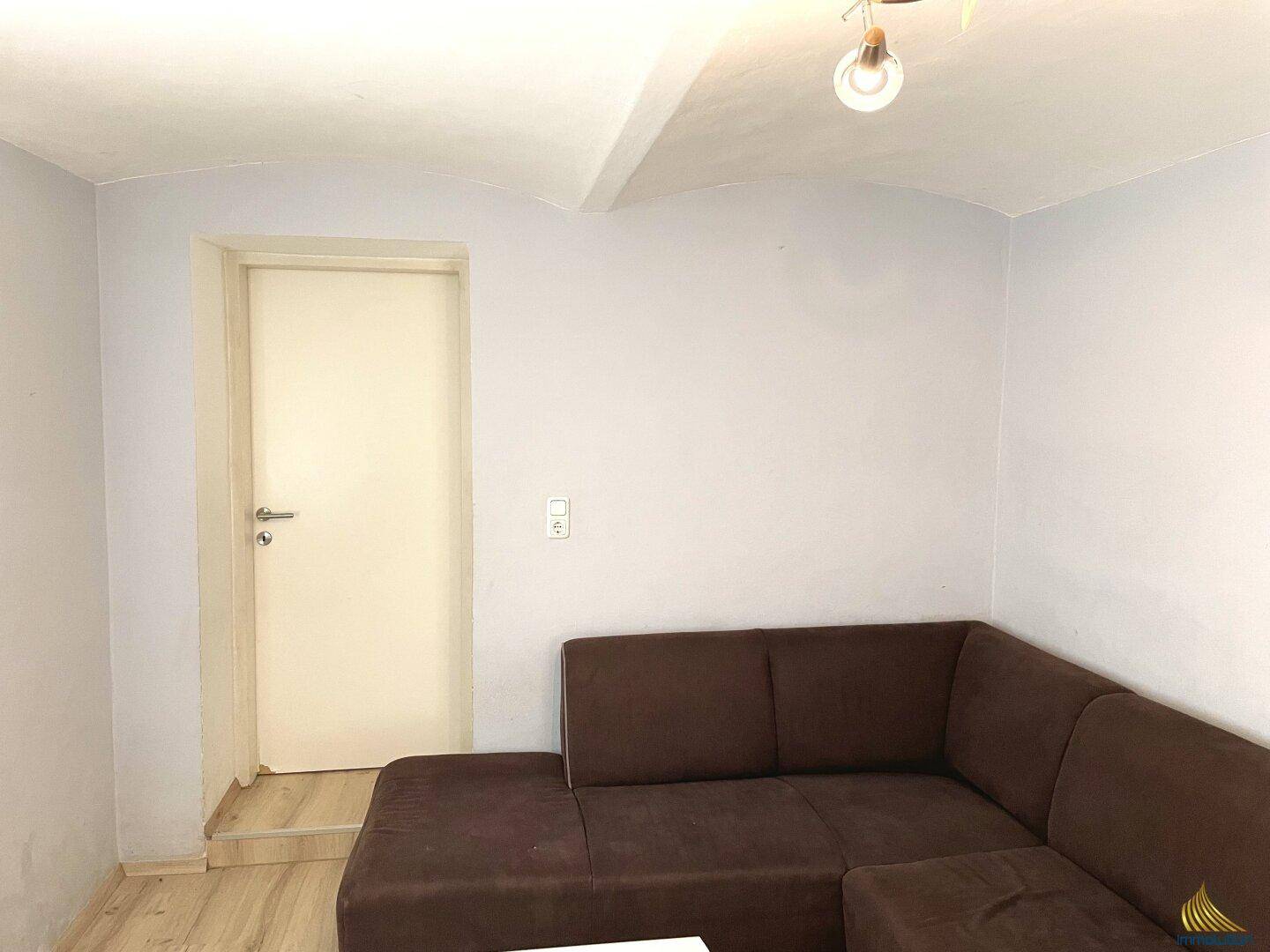 Wohnzimmer mit braunem Ecksofa und weiß gestrichenen Wänden.