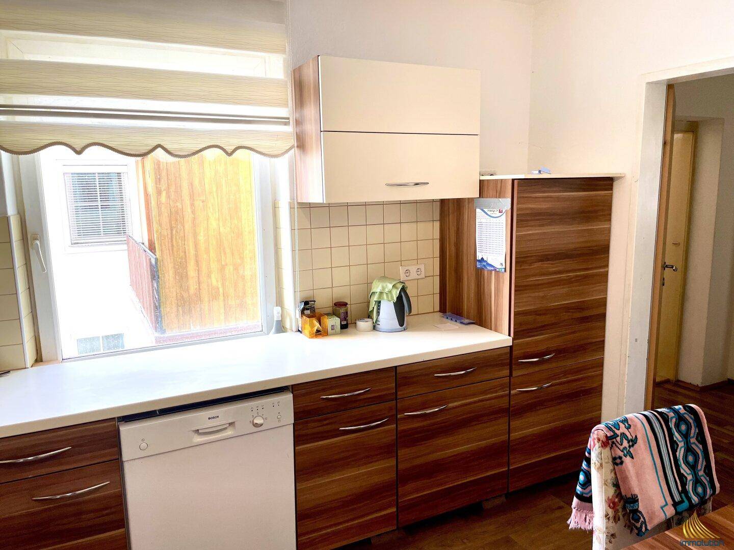 Küche mit Holzschränken, weißer Arbeitsplatte und Fenster mit Blick nach draußen.