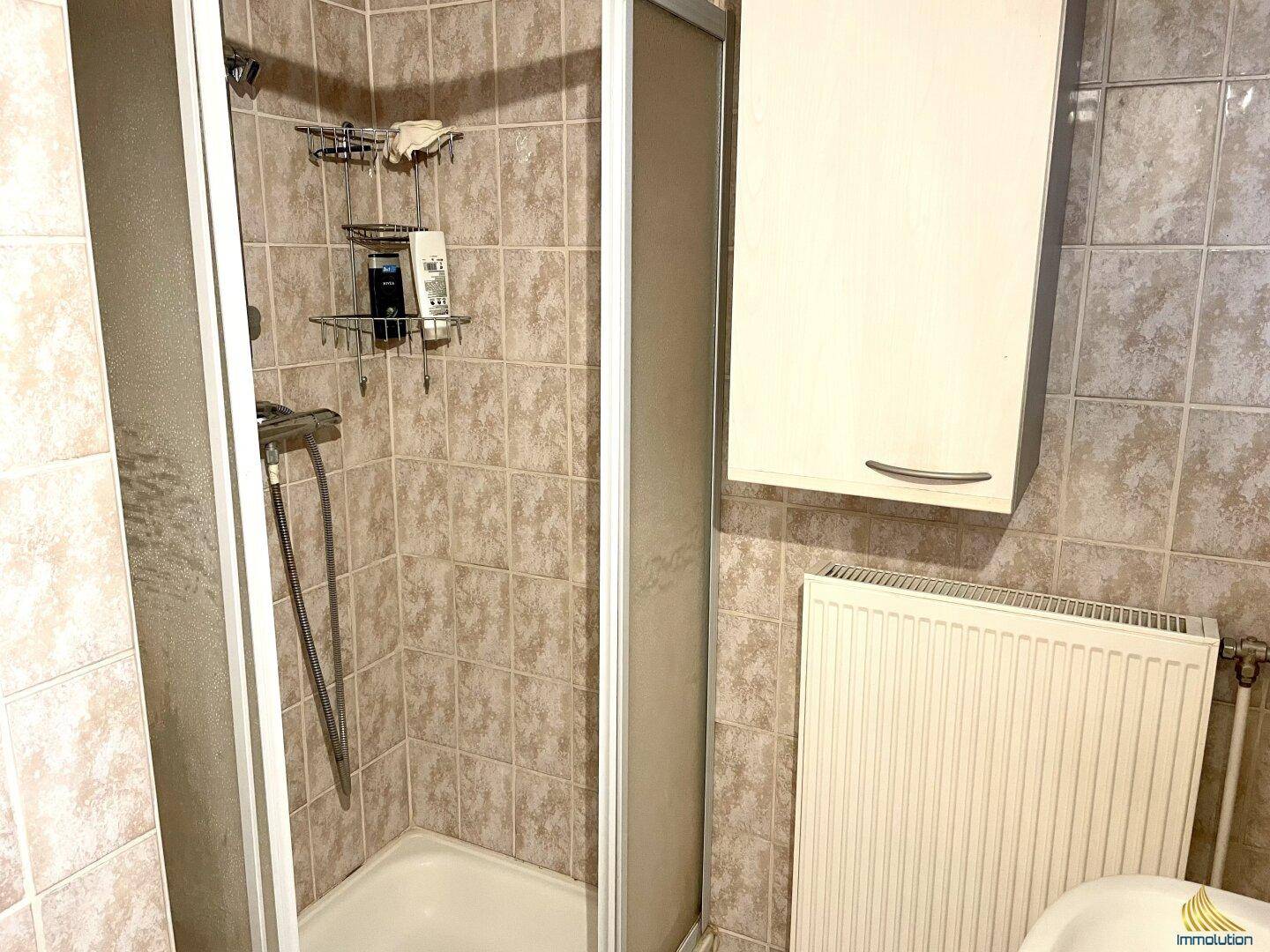 Badezimmer mit beigen Fliesen, Duschkabine und Heizkörper.