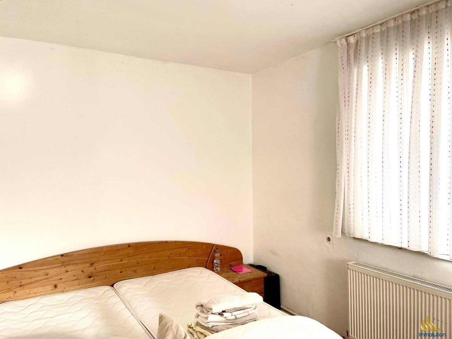 Schlafzimmer mit Doppelbett, Holzkopfteil und Fenster mit Vorhängen.