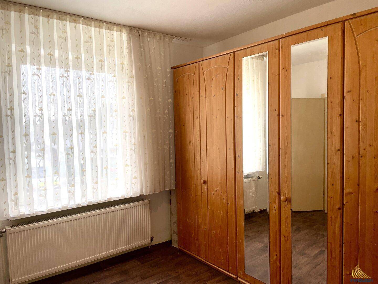 Schlafzimmer mit großem Holzschrank mit Spiegeltüren und Fenster.
