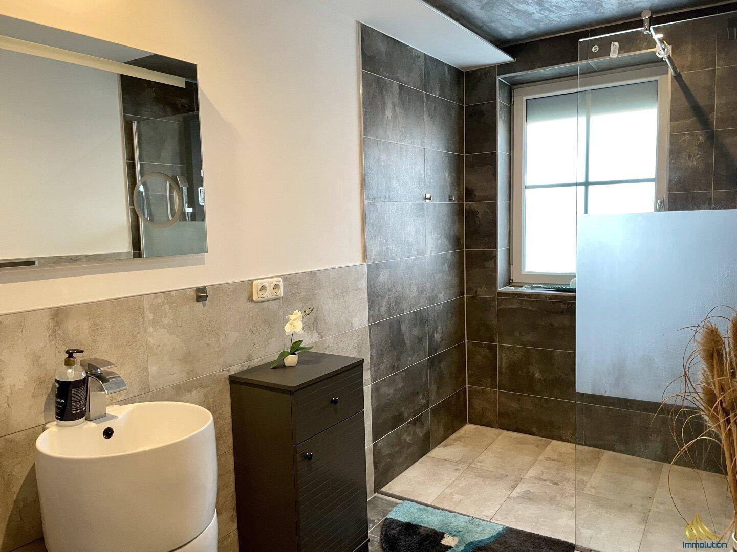 Modernes Badezimmer mit großer begehbarer Dusche, stilvollen Fliesen und einem Fenster für natürliche Belüftung.