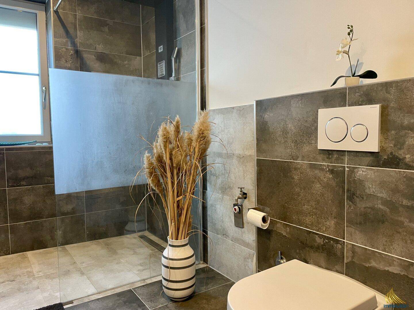 Badezimmer mit moderner Dusche, Wand-WC und eleganten Fliesen, ergänzt durch dekorative Elemente.