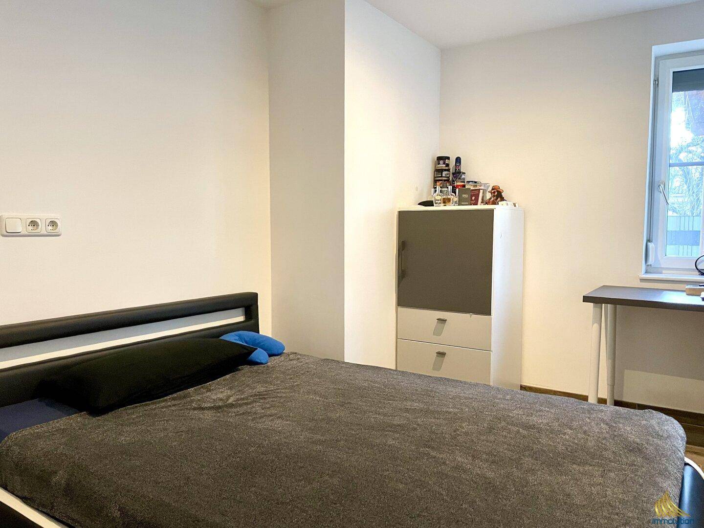 Helles Schlafzimmer mit Bett, Schreibtisch und Fenster, das viel Tageslicht hereinlässt.
