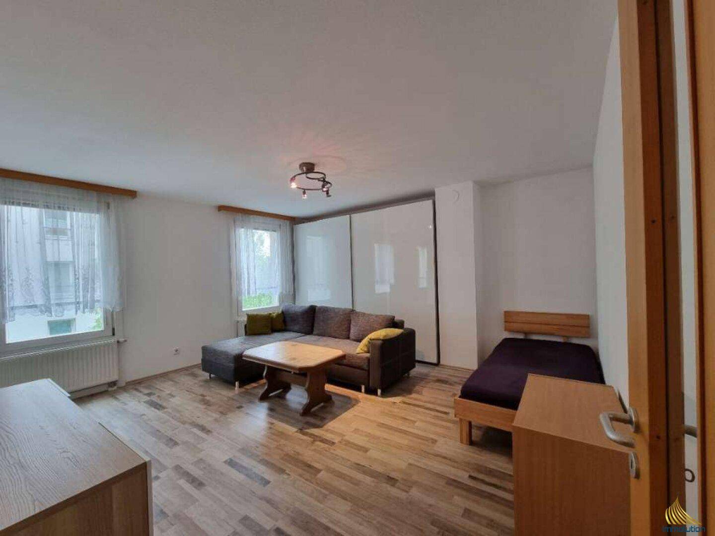 Geräumiges Wohnzimmer mit Schlafbereich, Sofa, Couchtisch und großem Einbauschrank.