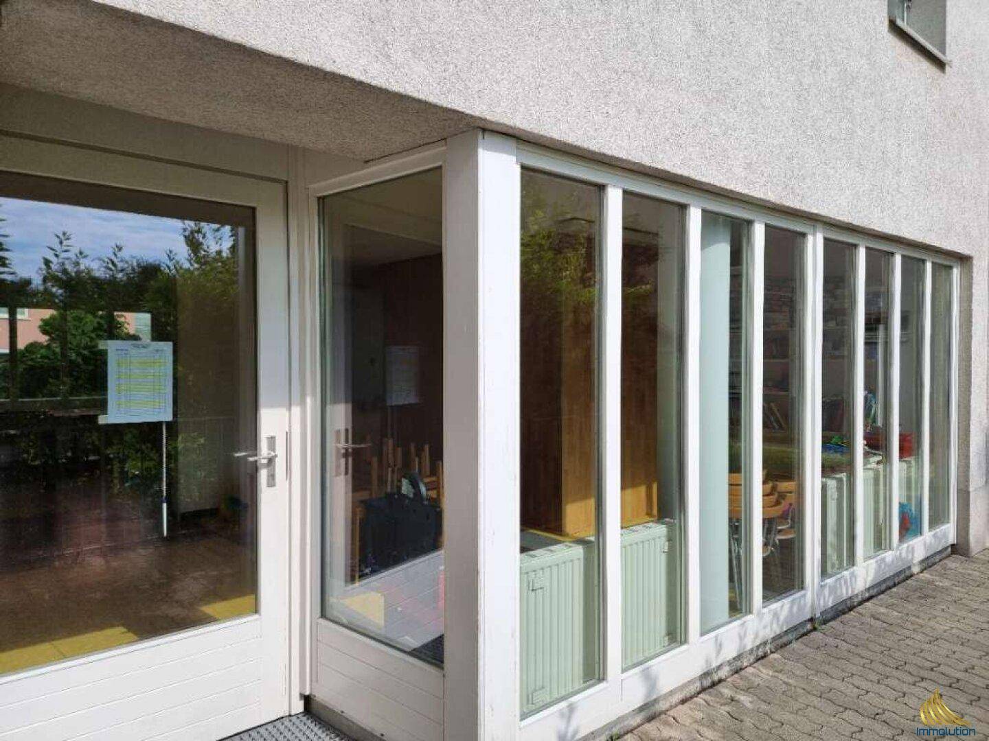 Außenansicht eines Wintergartens mit großen Fenstern und sichtbaren Heizkörpern, direkt am Gebäude.