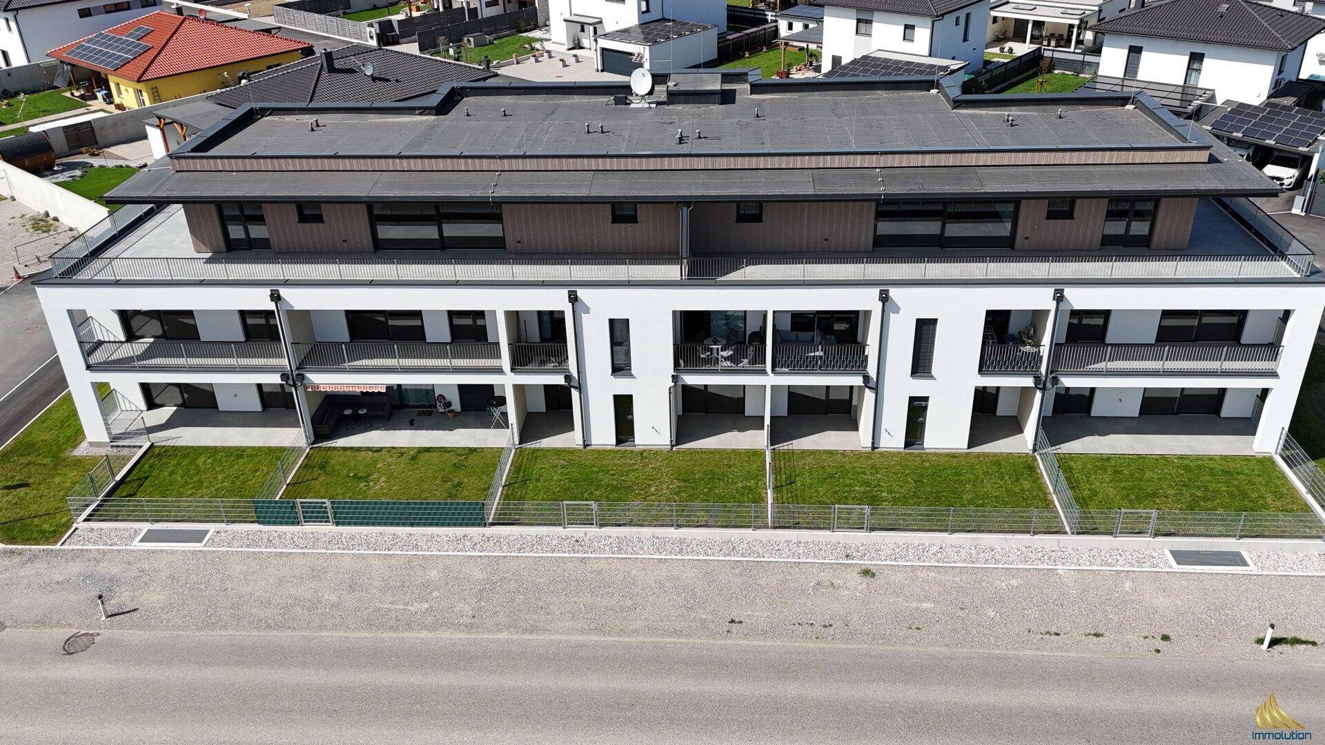 Moderne Wohnanlage mit weißer Fassade, mehreren Balkonen und privaten Gartenanteilen im Erdgeschoss.