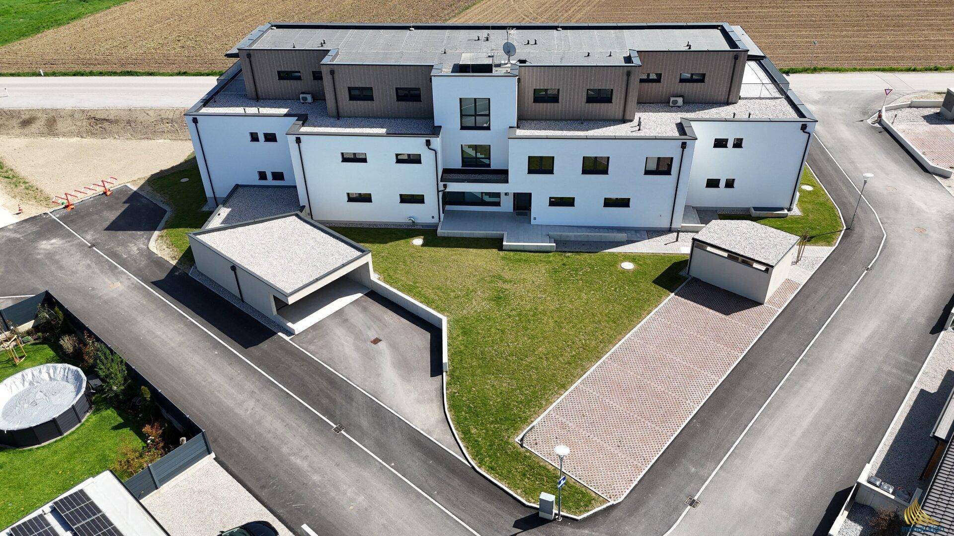 Luftaufnahme eines modernen Wohnkomplexes mit mehreren Gebäuden, Parkplätzen und Grünflächen.