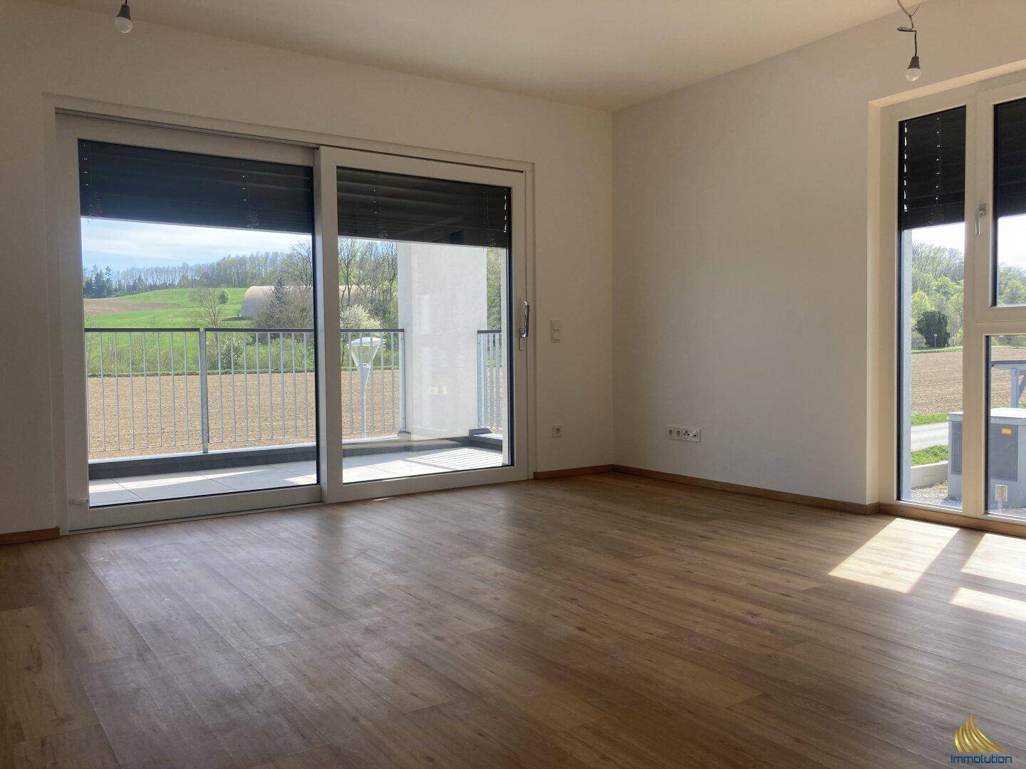 Helles Wohnzimmer mit großen Schiebetüren zum Balkon und weitem Blick ins Grüne. Der Boden ist mit Laminat ausgelegt.