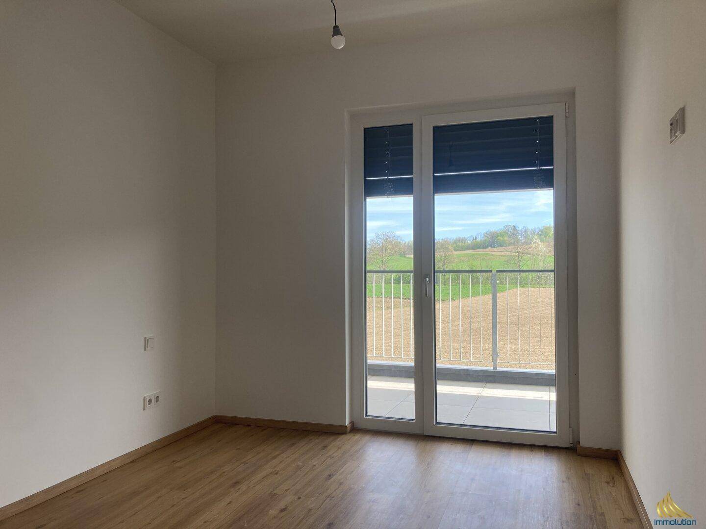 Schlafzimmer mit Zugang zum Balkon und schöner Aussicht auf die umliegende Landschaft. Der Raum ist hell und leer.