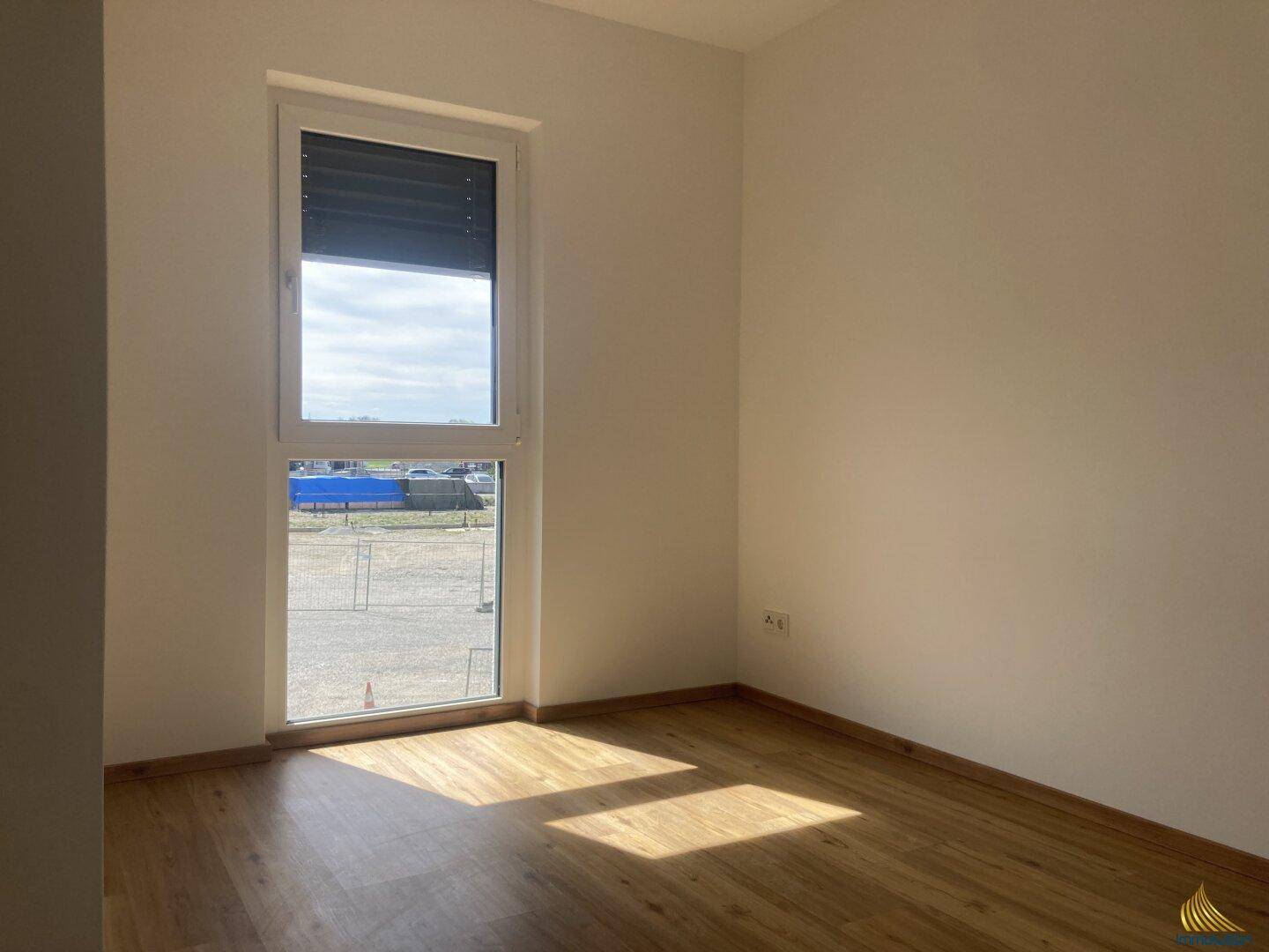 Helles Zimmer mit einem großen Fenster, das viel Tageslicht hereinlässt. Der Boden ist mit Laminat ausgelegt.