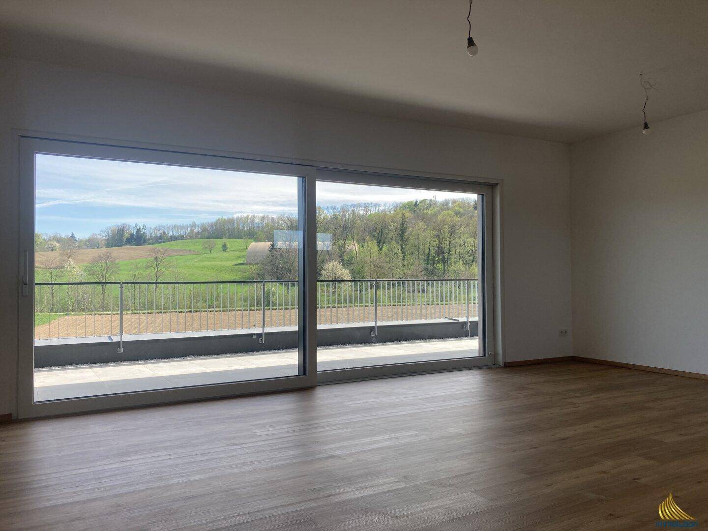 Heller Wohnraum mit großen Schiebetüren, Holzboden und weitem Blick ins Grüne.