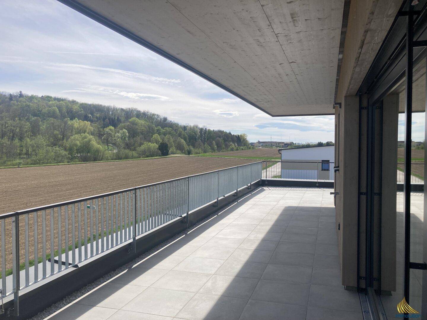 Geräumige Terrasse mit weitem Blick über Felder und grüne Hügel unter strahlendem Himmel.