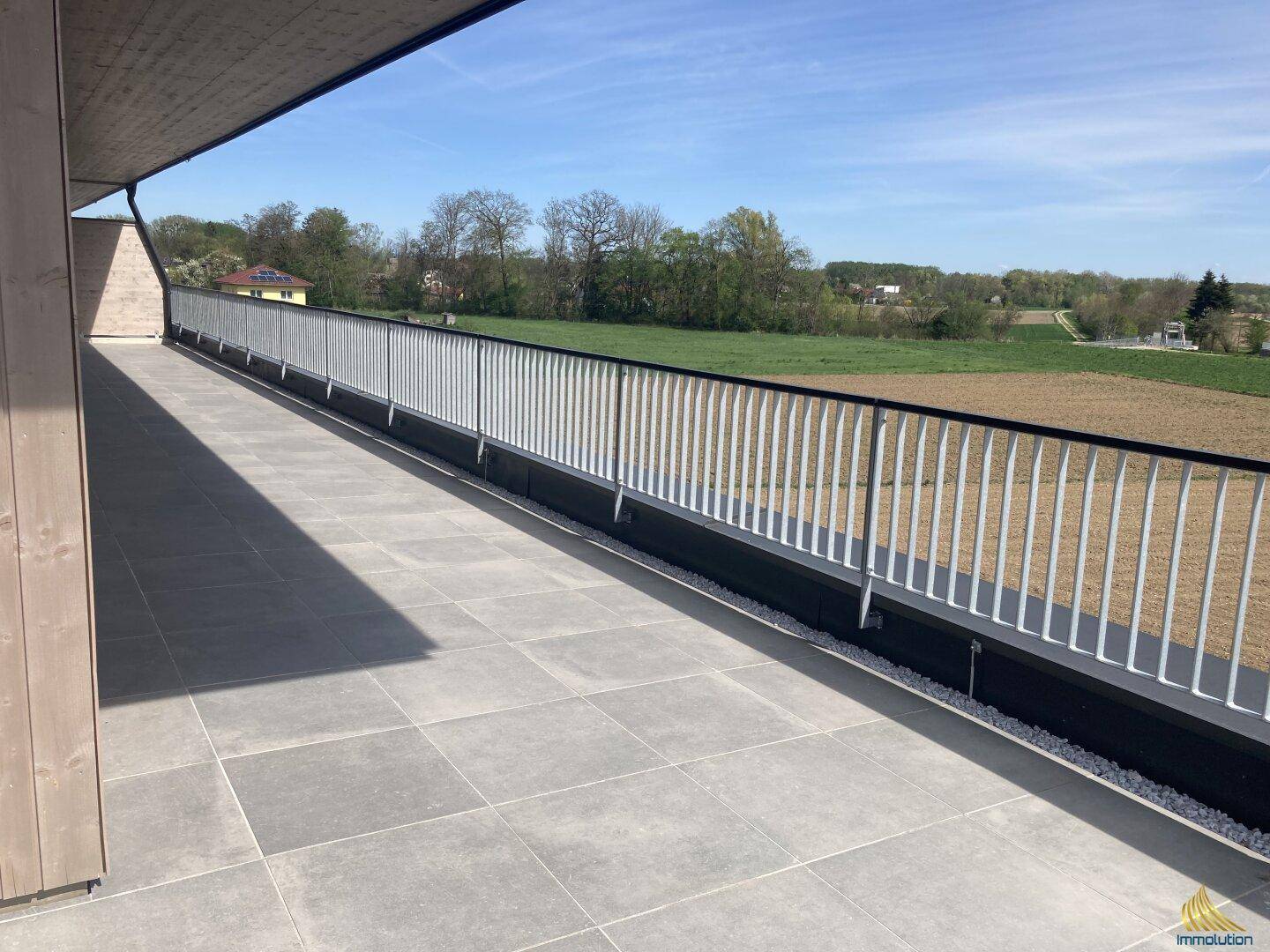 Weitläufige Terrasse mit Metallgeländer und freiem Blick auf die umliegende Natur und Felder.