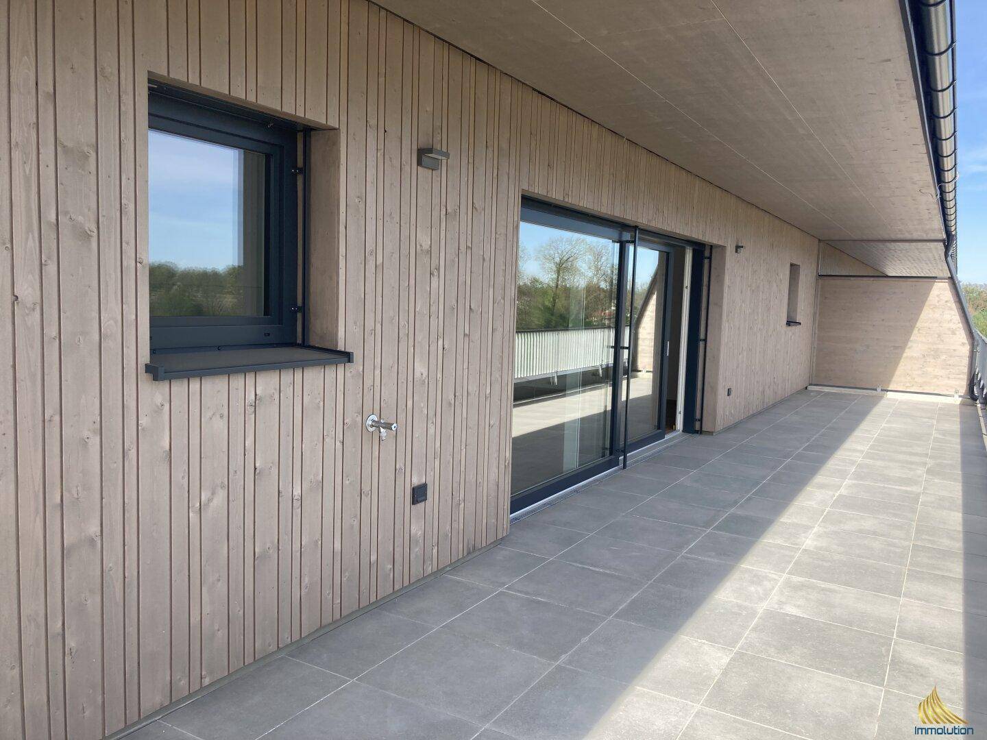 Teilansicht der gefliesten Terrasse mit Holzverkleidung und Zugang durch große Schiebetüren.