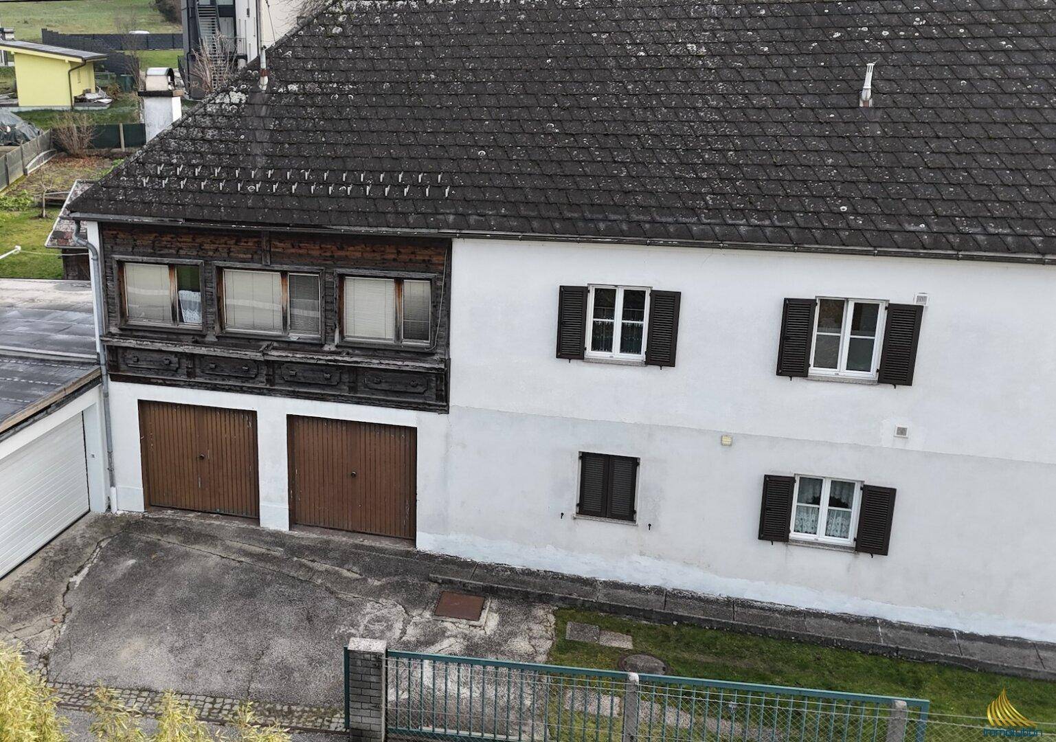 Rückansicht des Gebäudes mit zwei Garagentoren und einem Satteldach, umgeben von Grünflächen.