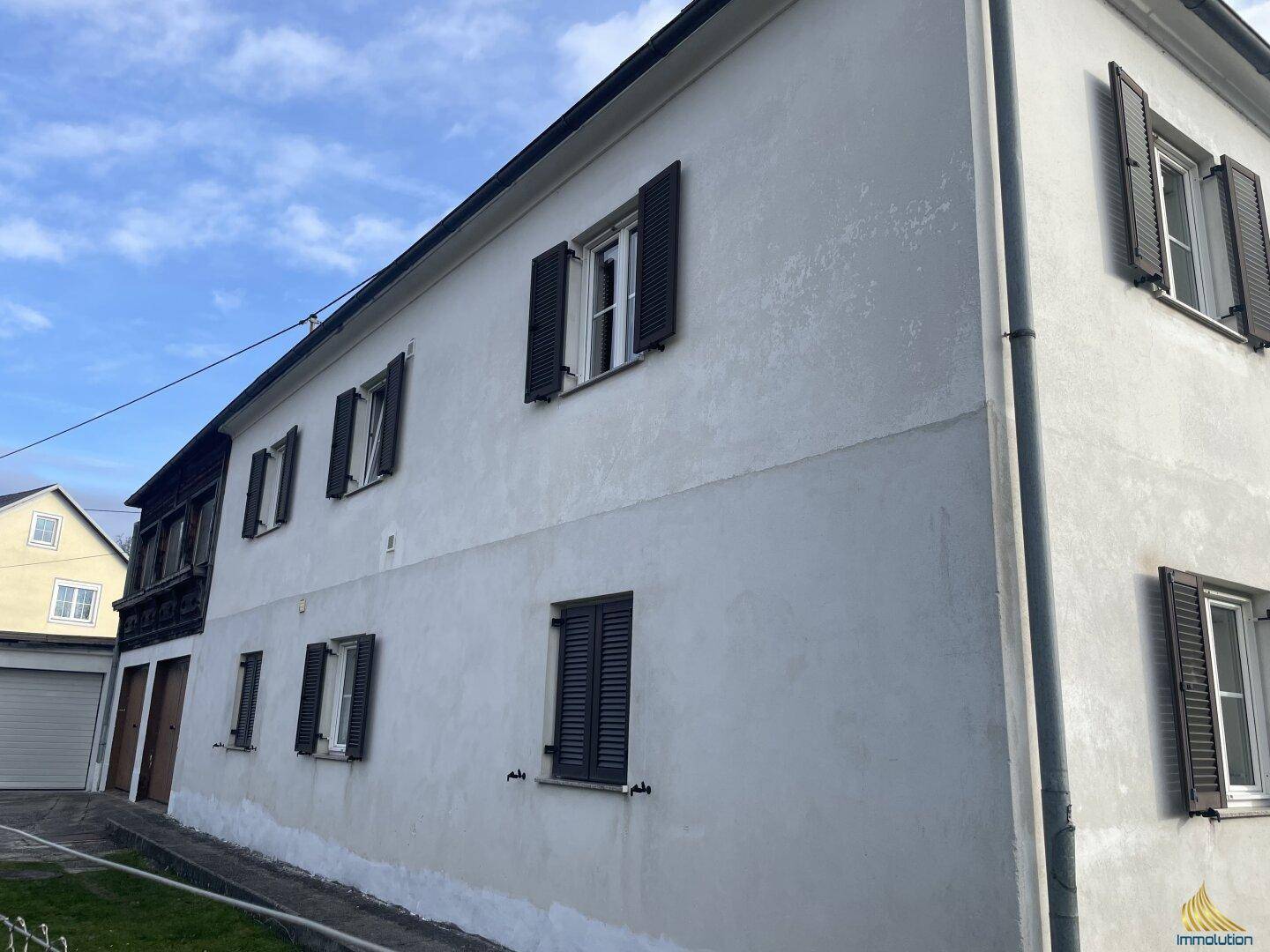 Seitenansicht eines älteren Gebäudes mit weißer Fassade und dunklen Fensterläden.