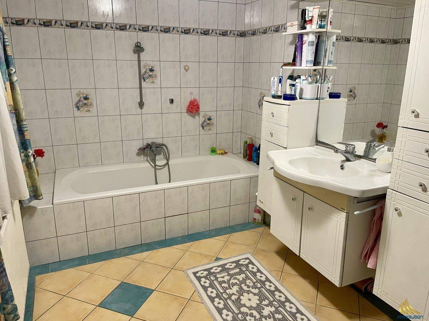 Badezimmer mit Badewanne, Einzelwaschbecken und Fliesen im Stil der 80er Jahre.