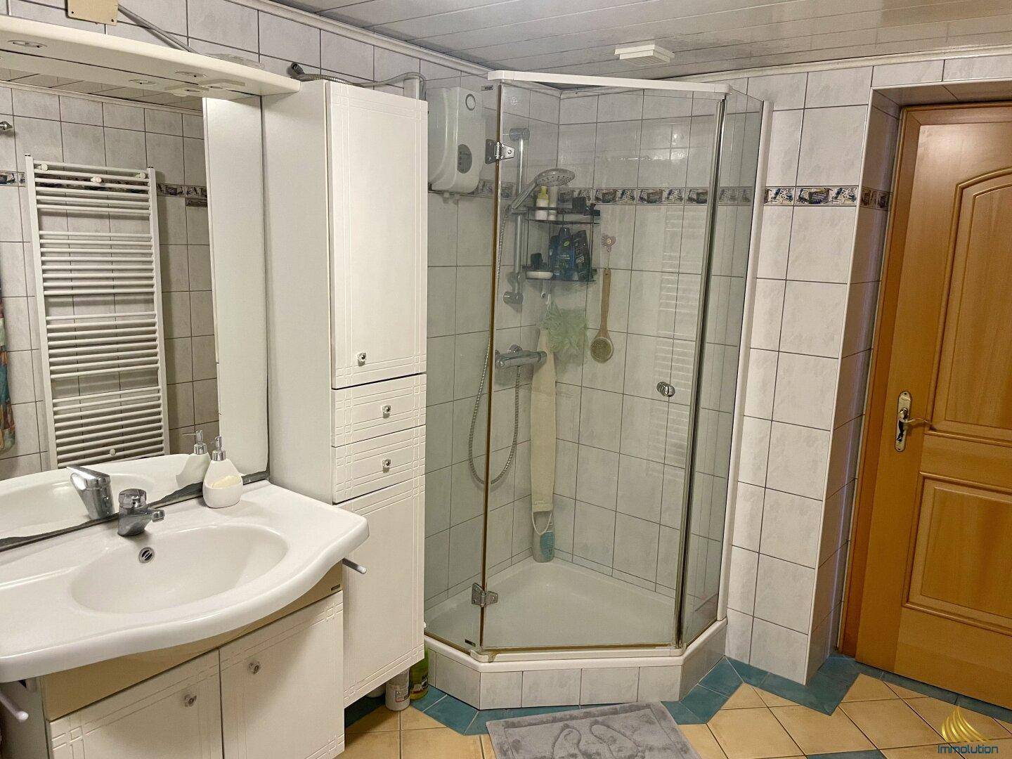 Badezimmer mit Duschkabine, Einzelwaschbecken und Fliesen im Stil der 80er Jahre.