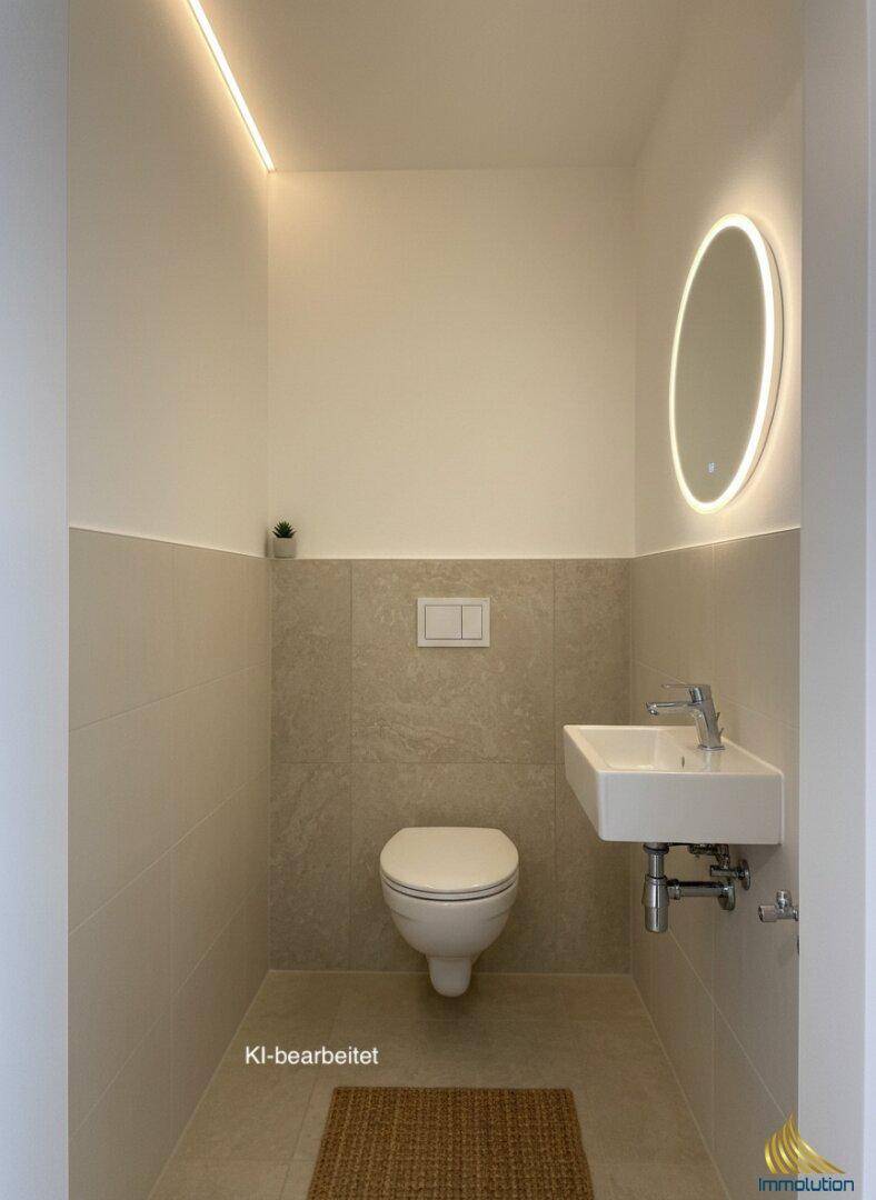 Helles Gäste-WC mit Wand-WC, kleinem Waschbecken und beleuchtetem Spiegel.